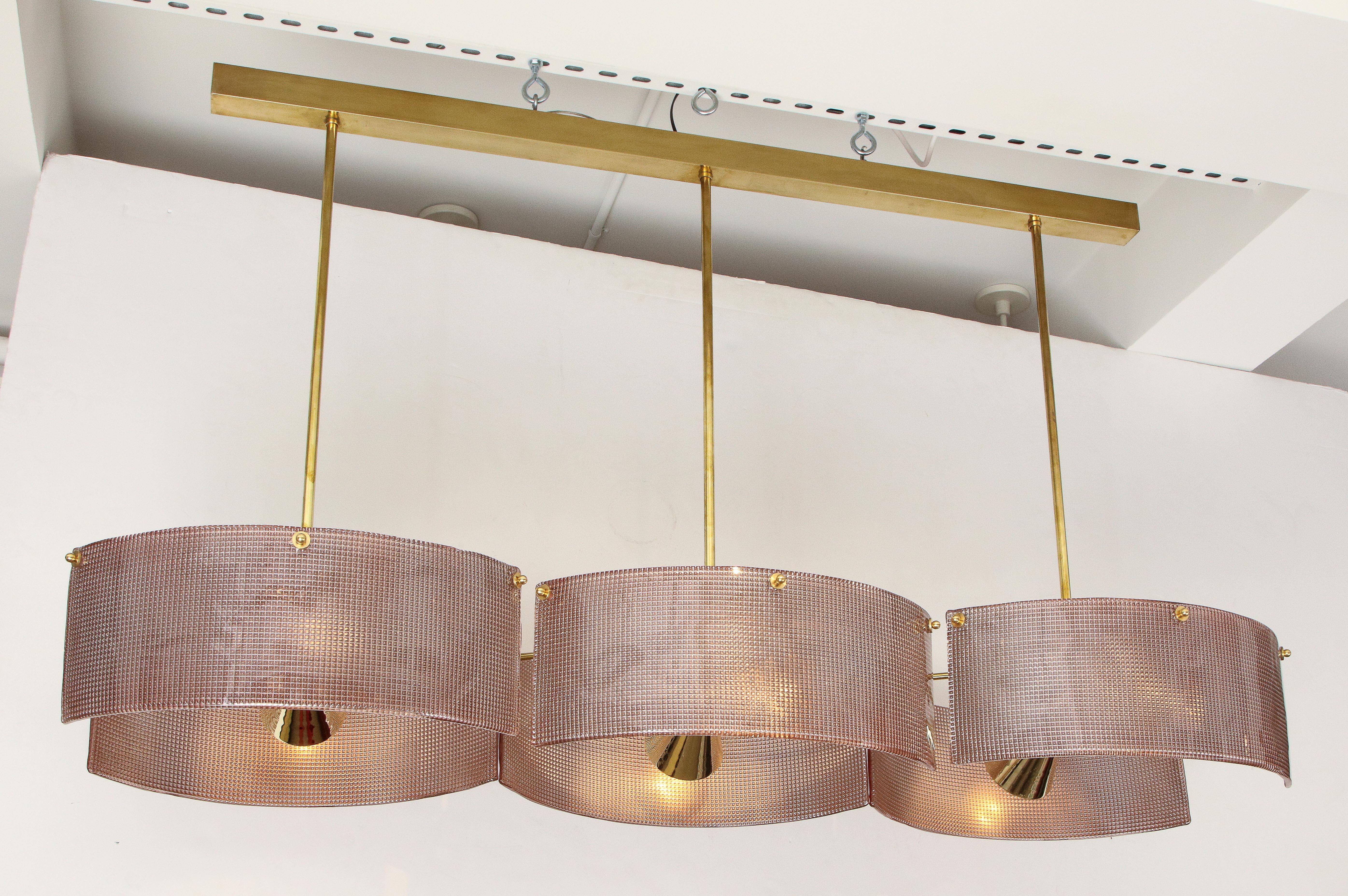 This sophisticated Italian chandelier is made of brass and hand casted pink blush colored Murano glass. It consists of six curved pieces of textured, blush Murano glass shields or plates with suspended brass spot lights reflecting light off of each