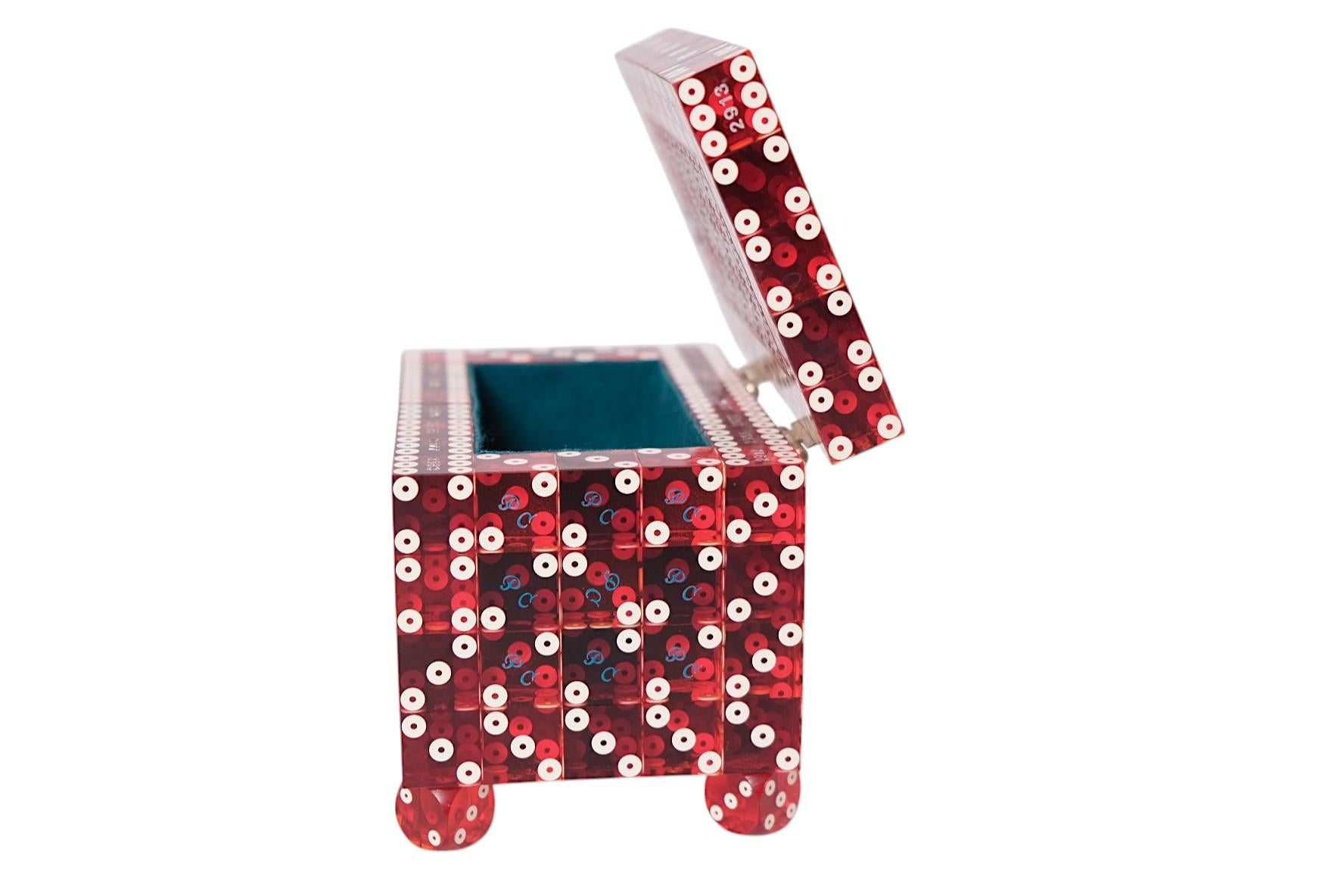 Une boîte artisanale unique fabriquée entièrement à partir de dés de casino vintage en acrylique rouge. La boîte repose sur des pieds en dés assortis et s'ouvre sur des charnières en laiton pour révéler un intérieur tapissé de velours sarcelle. Un