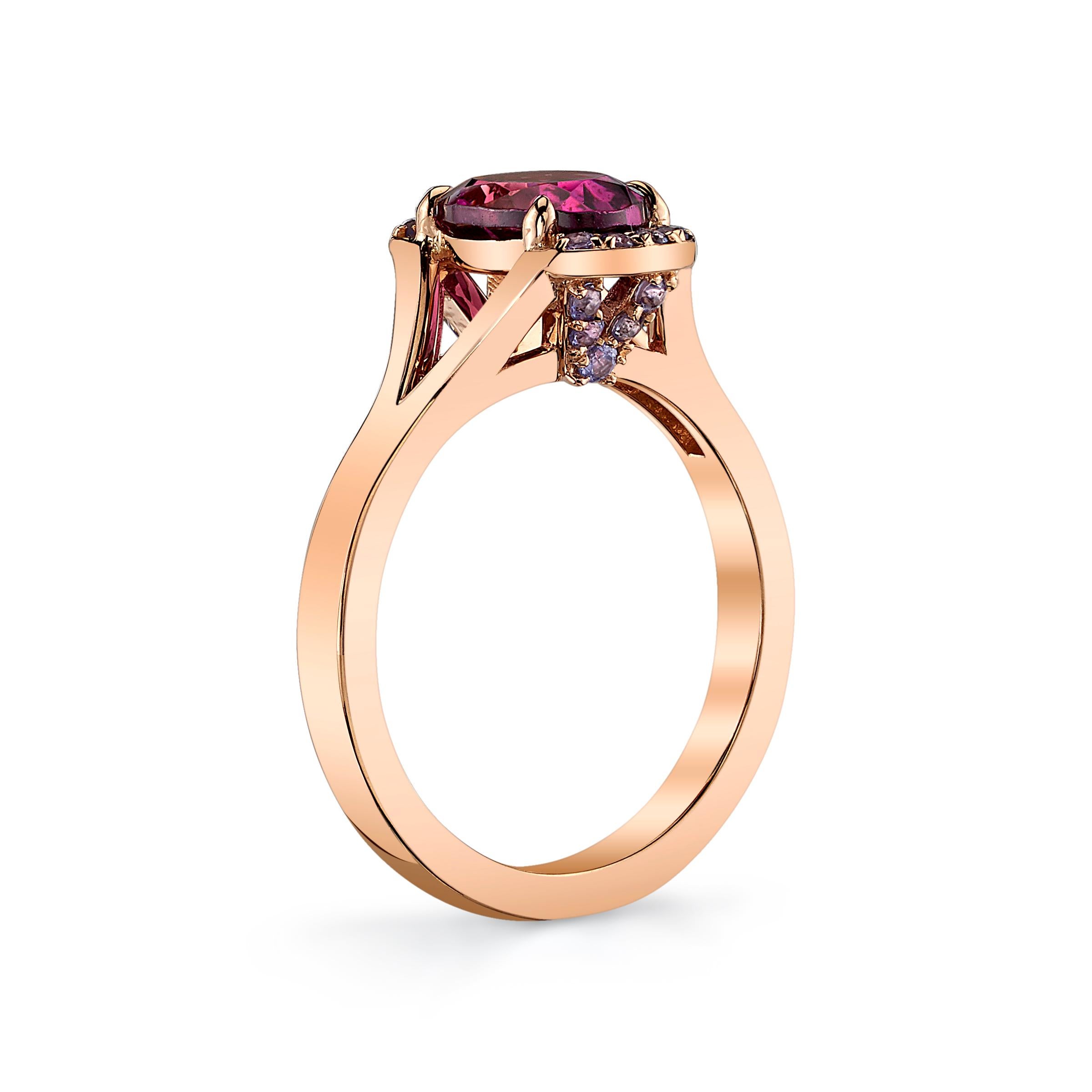 Un granato ovale di rodolite di 1,57 carati è sostenuto da quattro griffe e accentuato da piccole tanzaniti per alcuni dettagli della vista superiore e laterale. L'ispirazione per questo anello è venuta da un'opera d'arte in cui il rosa-viola era