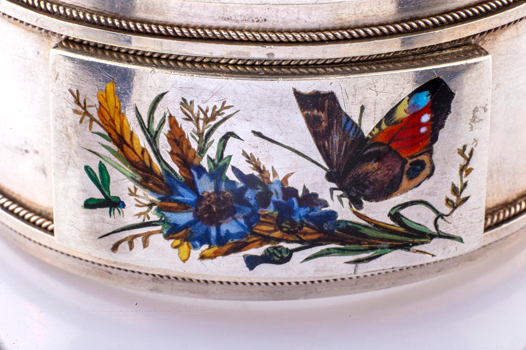 Un raro esempio di bracciale d'argento vittoriano con una placca allegata raffigurante una farfalla arancione dipinta a mano in blu e marrone che sta per posarsi su uno spruzzo di fiori. La farfalla ha compagnia perché un'ape è attratta dallo stesso