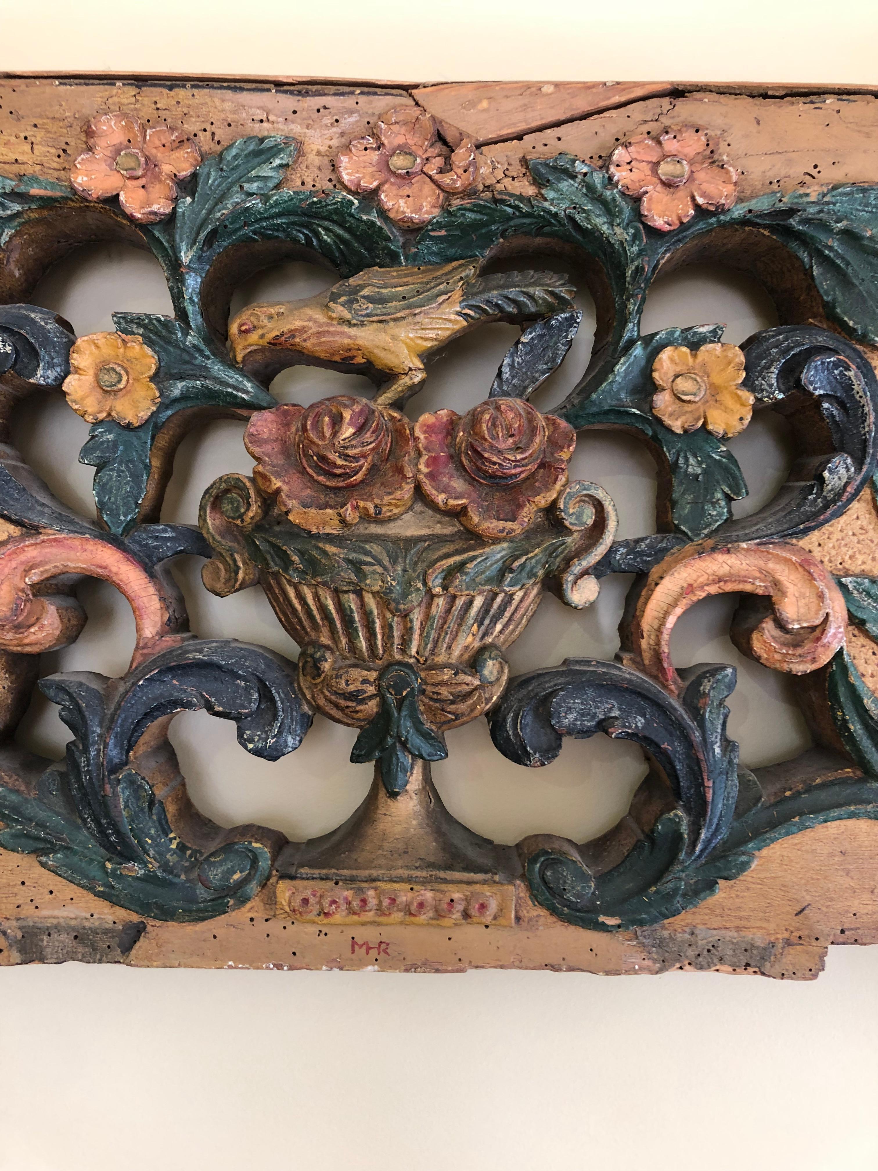 An eye catching architectural carved wood found object wall sculpture, probably once an overhead door adornment, having carved flowers in an urn with bird on top. Fabulous squiggly hardware on the front and foliage.
