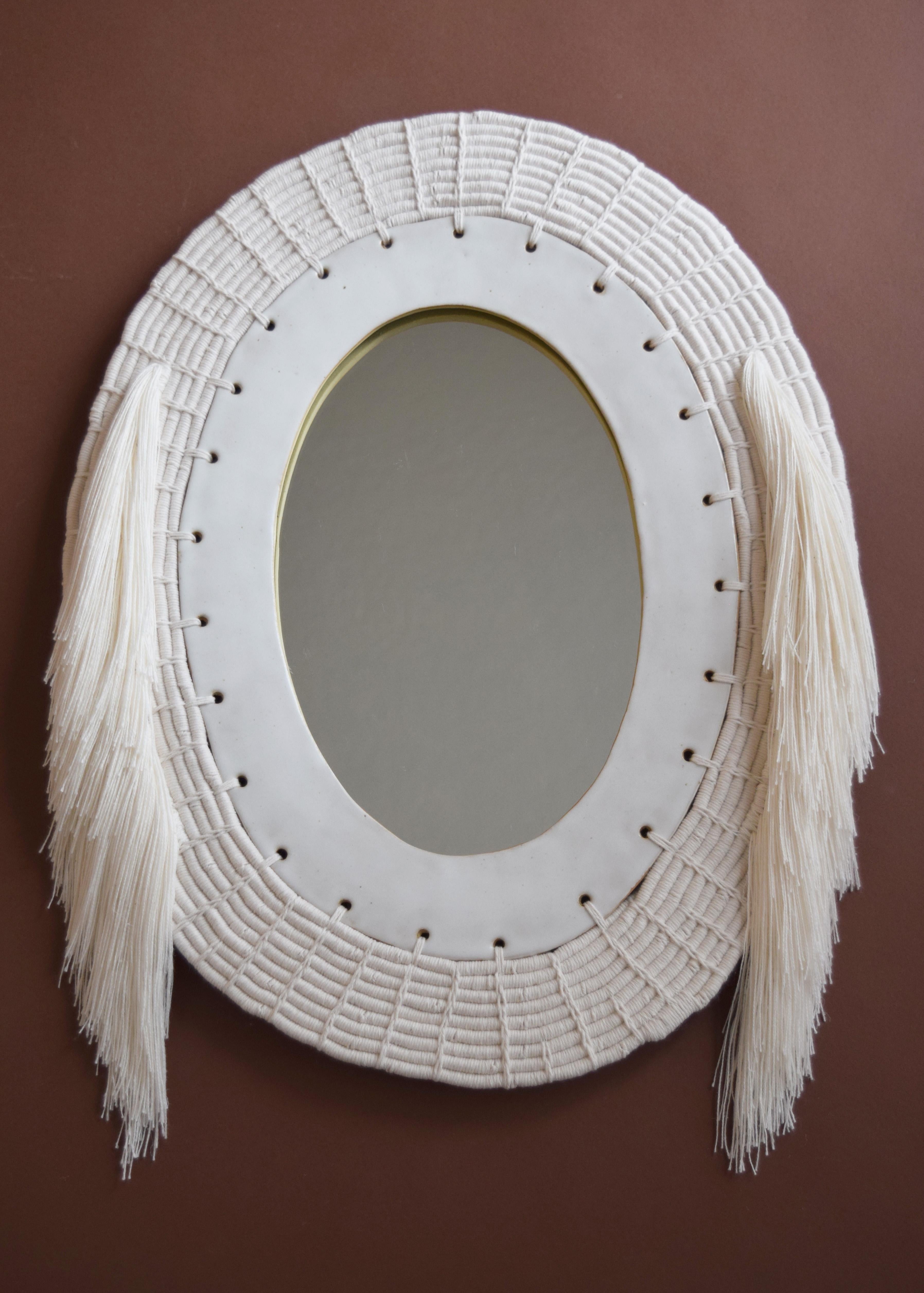 One of a kind mirror #714 by Karen Gayle Tinney

Decorative mirror with hand formed stoneware frame glazed in satin white. The frame exterior is woven in white cotton with white cotton fringe, using a coiling technique which is a signature of the