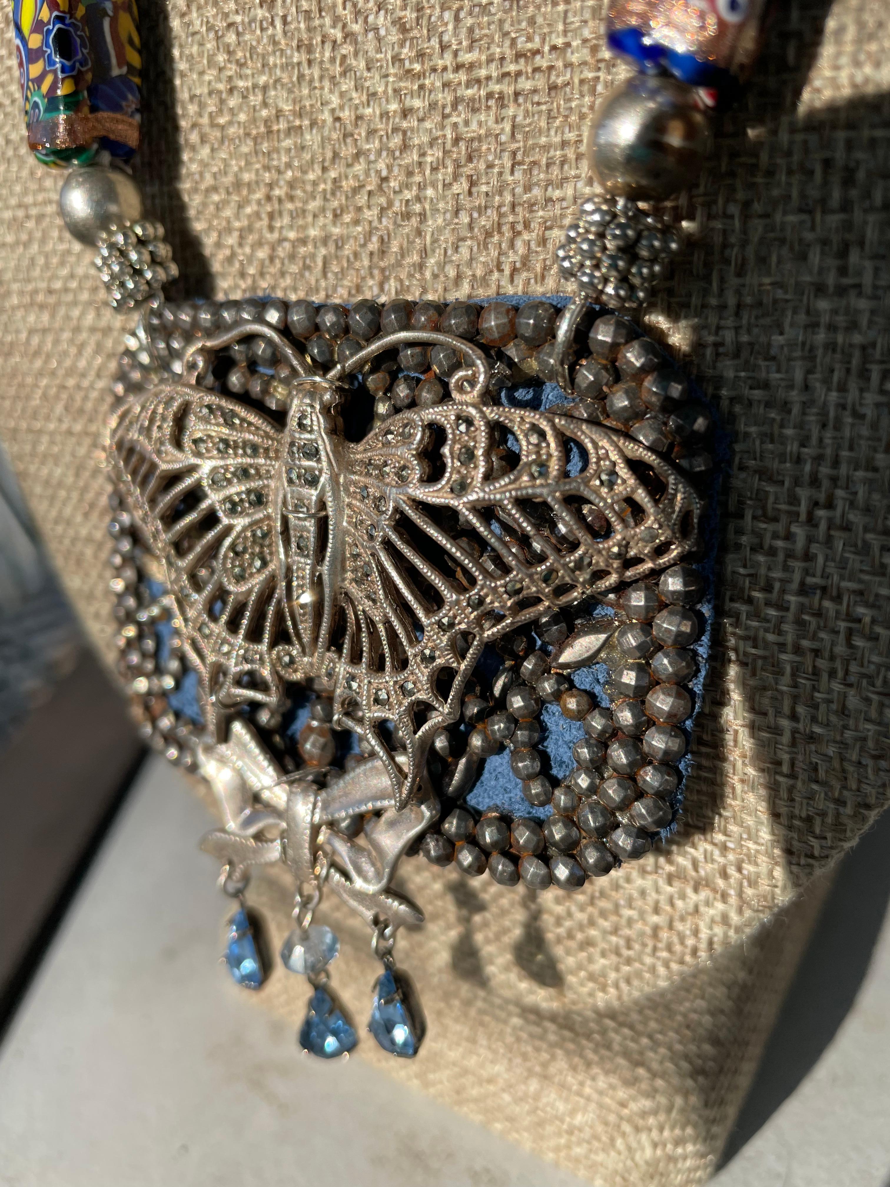 From Lorraine’s Bijoux an original,one of a kind,handmade,statement necklace with a vintage French metal buckle,vintage sterling and marcasite butterfly brooch. A vintage sterling bow brooch is part of the centerpiece pendant.Blue leather is used as