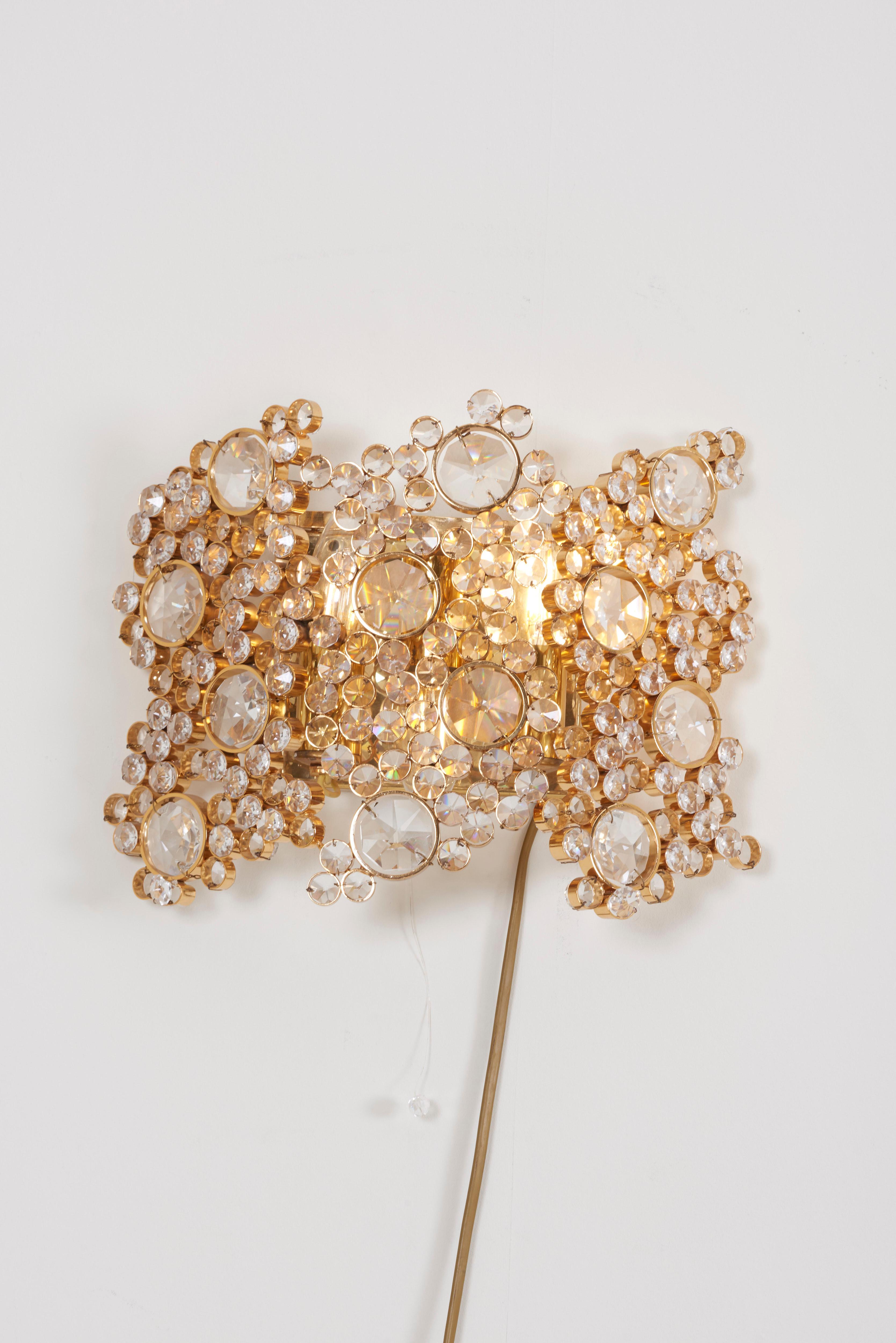One of four outstanding Palwa wall lamps from the 1970s. The gold-plated brass frames are encrusted with high quality diamonds like crystals. The chandeliers are handmade and in excellent condition and float every room in a beautiful warm light. It