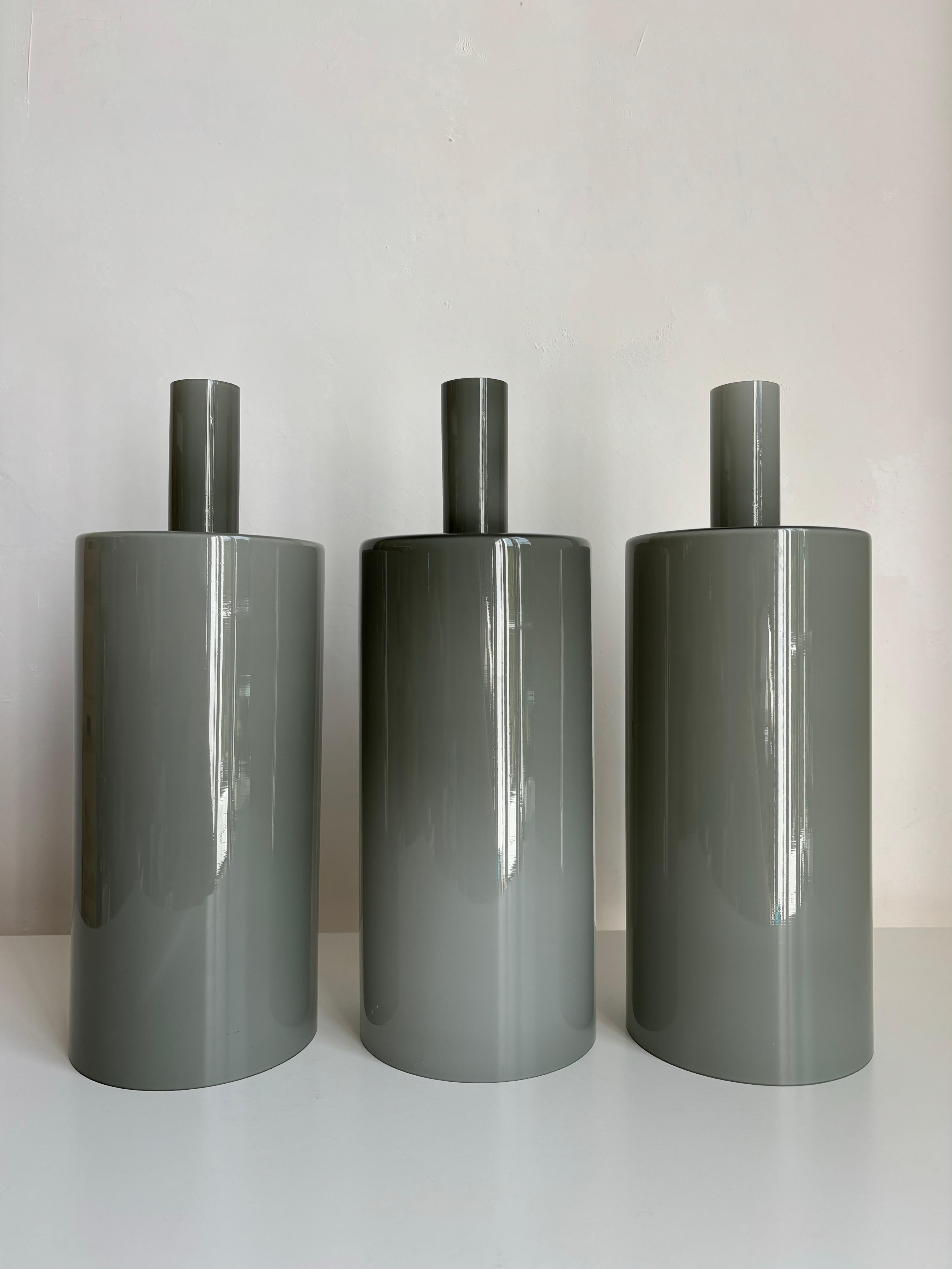 Uno dei tre eleganti pendenti danesi in vetro artistico grigio caldo della metà del secolo scorso realizzati dall'acclamato designer Johannes Hammerborg (1920-1982) per Fog & Mørup con la danese Holmegaard. Il modello si chiama Pisa (E 2345) ed è