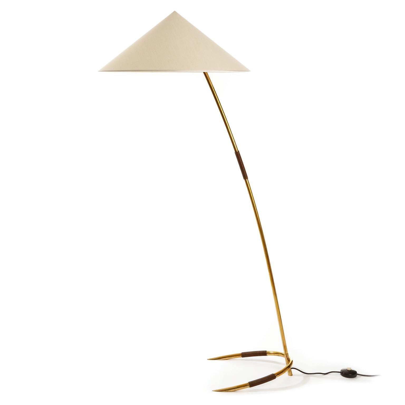 One of two gorgeous floor lights by Rupert Nikoll, Austria, manufactured in midcentury, circa 1960 (late 1950s or early 1960s).
Only one light is available.
A cone shaped and ivory toned lamp shade sits on a solid brass stand with a plastic string