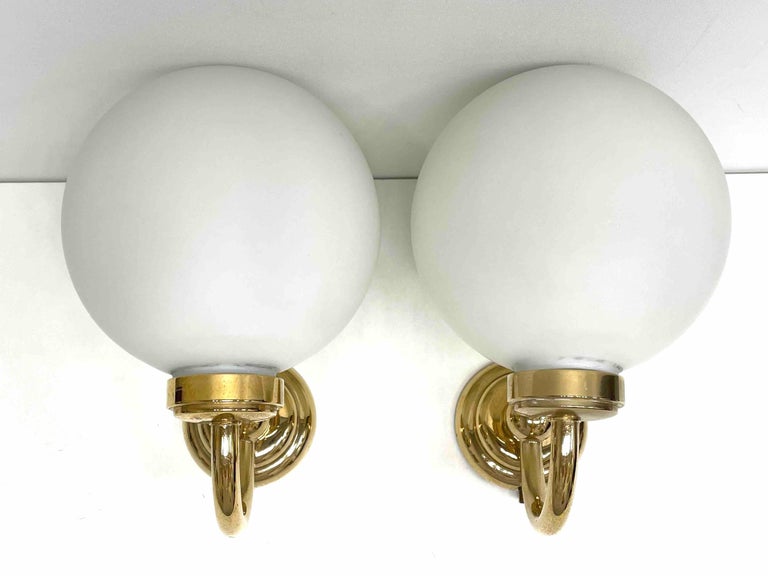 Pair of Art Deco style brass and milk glass sconces, made by Keuco Lights, Germany, each fixture requires one European E14 candelabra bulb, up to 40 watts. The wall lights have a beautiful brass frame and give each room an eclectic statement. 
