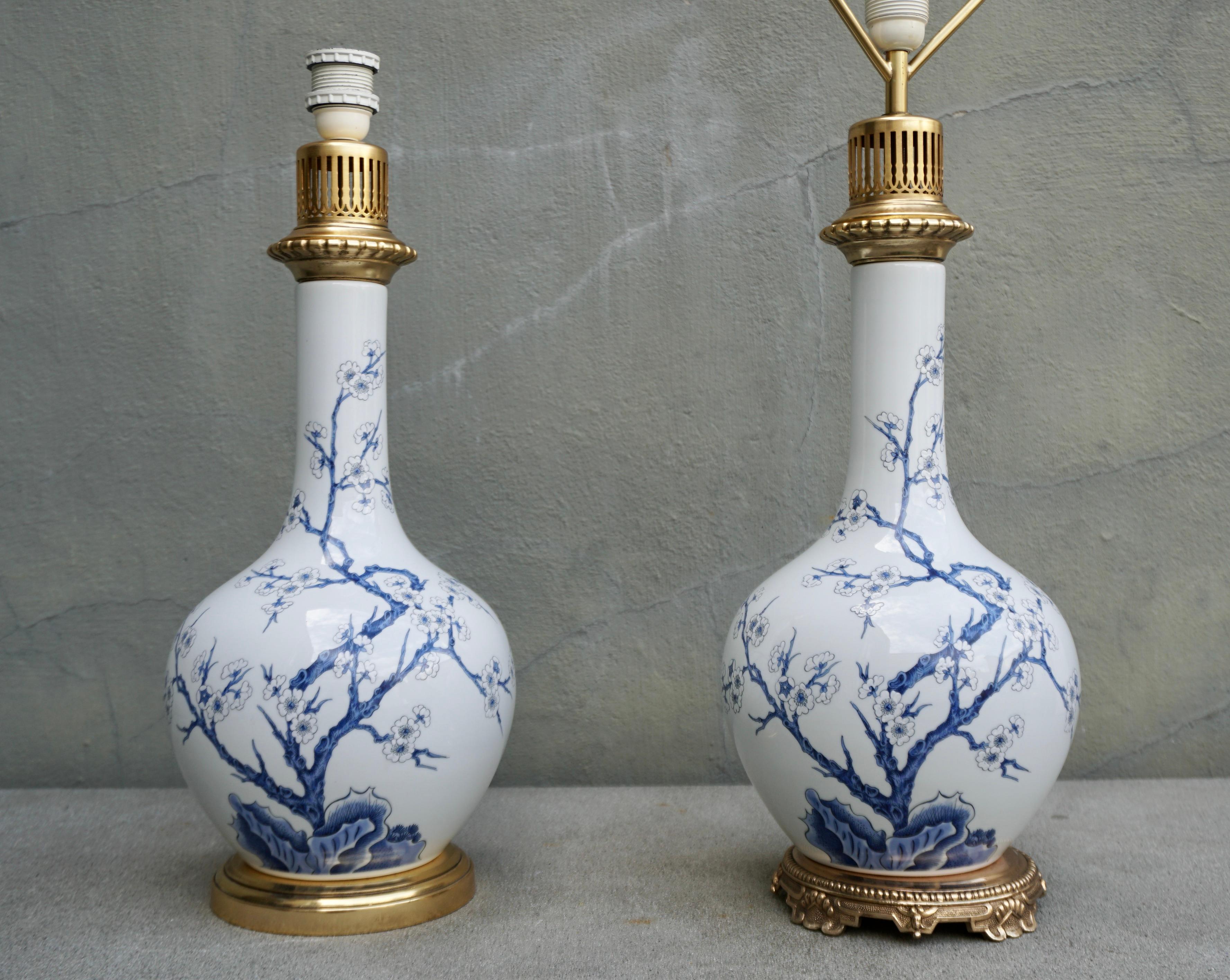Two 1950s Chinese style blue and white porcelain table lamp with floral decoration and bronze base. 
Each lamp decorated with meandering branchwork and cherry blossoms; underside with under-glaze blue stamp 'Porcelaine De Paris, France, Fondee en