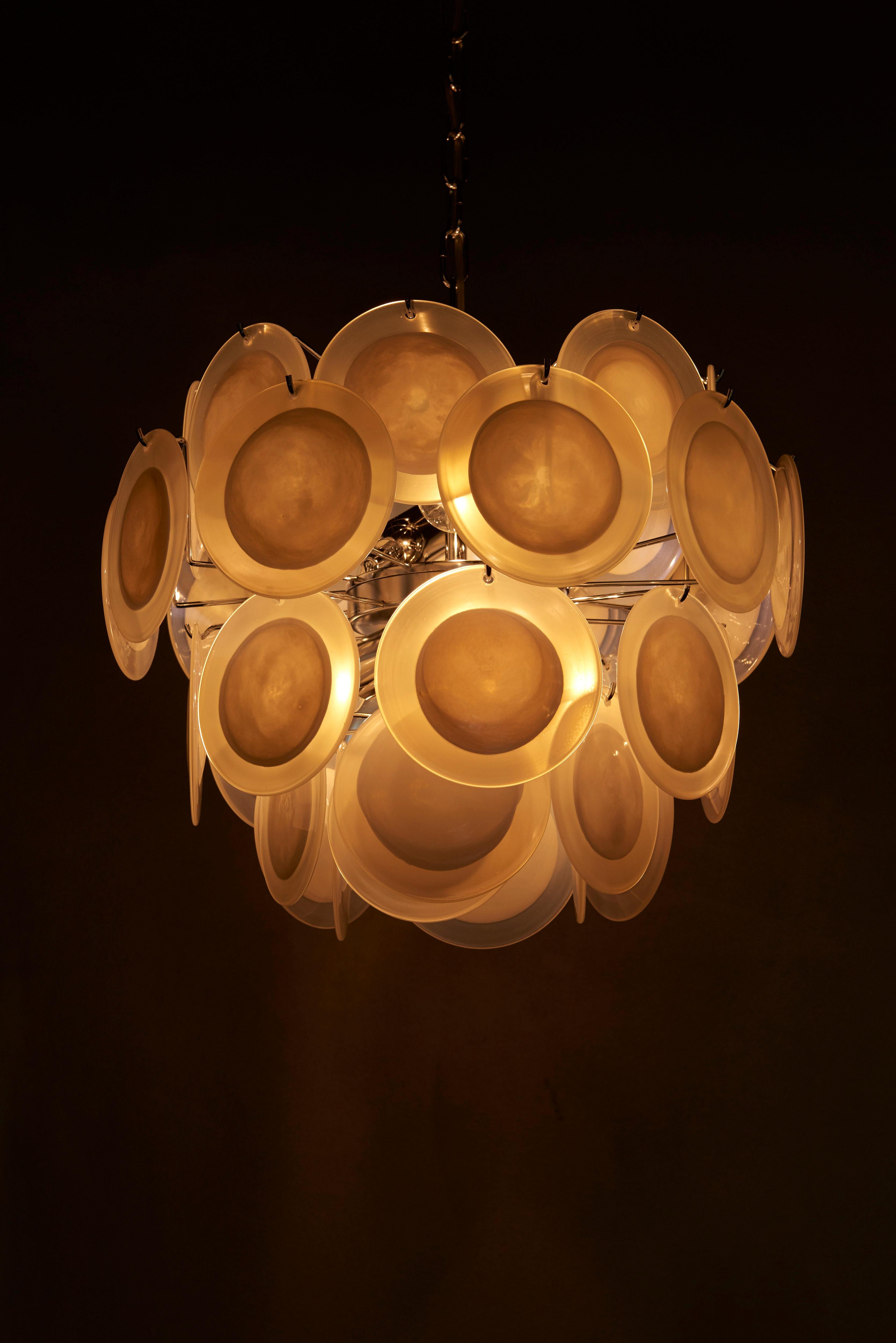 Very nice white iridescent Murano glass disc chandelier attributed to Vistosi. The chandelier is a perfect eyecatcher in every room. 5 x E27 bulbs. Two pieces available. 

To be on the safe side, the lamp should be checked locally by a specialist