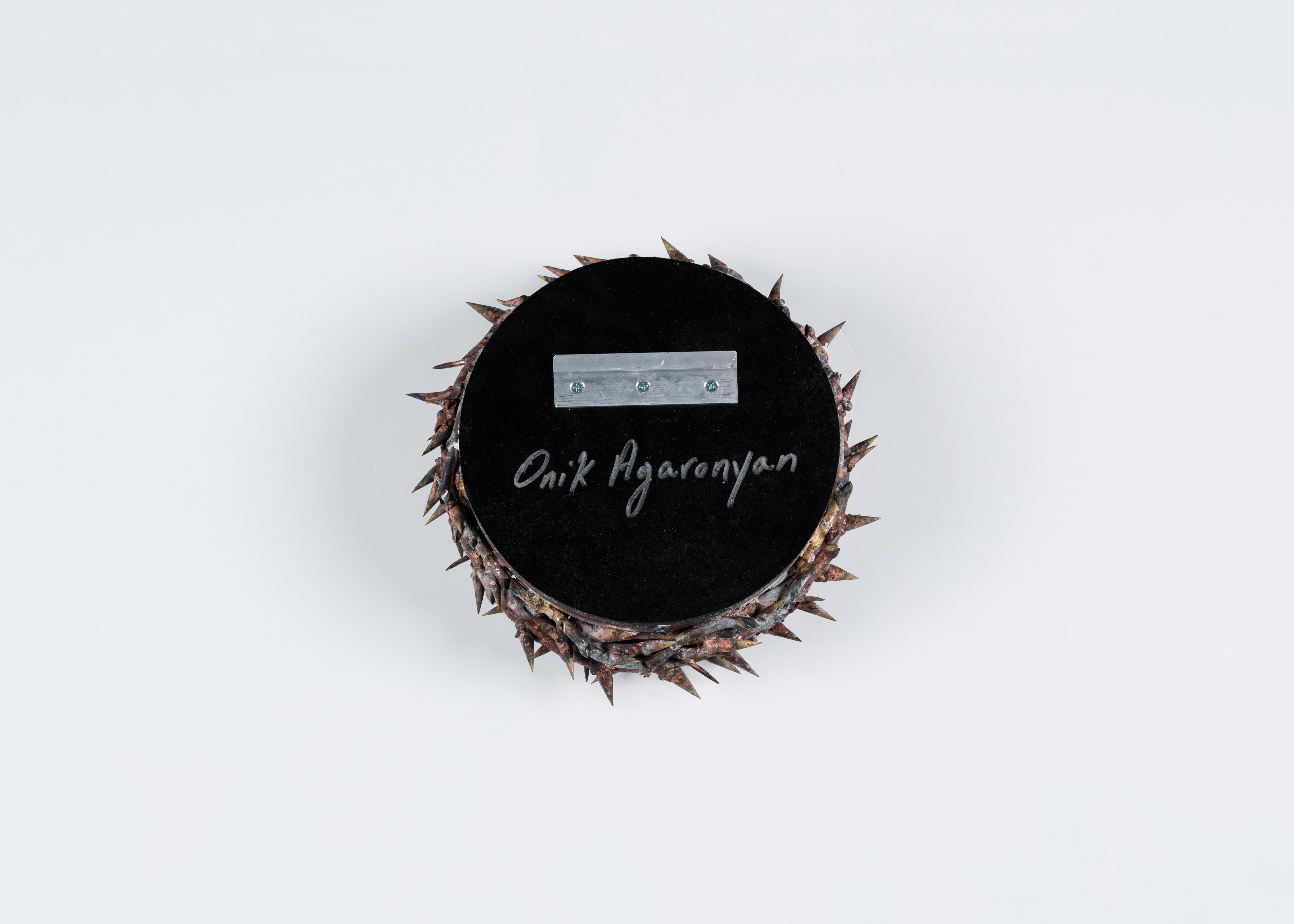 Signed: Onik Agaronyan

This sculptural mirror, with its roughly finished brass and copper frame, evokes the brutality of the crown of thorns worn at the crucifixion. Reflected in the mirrored glass at center, the thorns even seem to multiply.