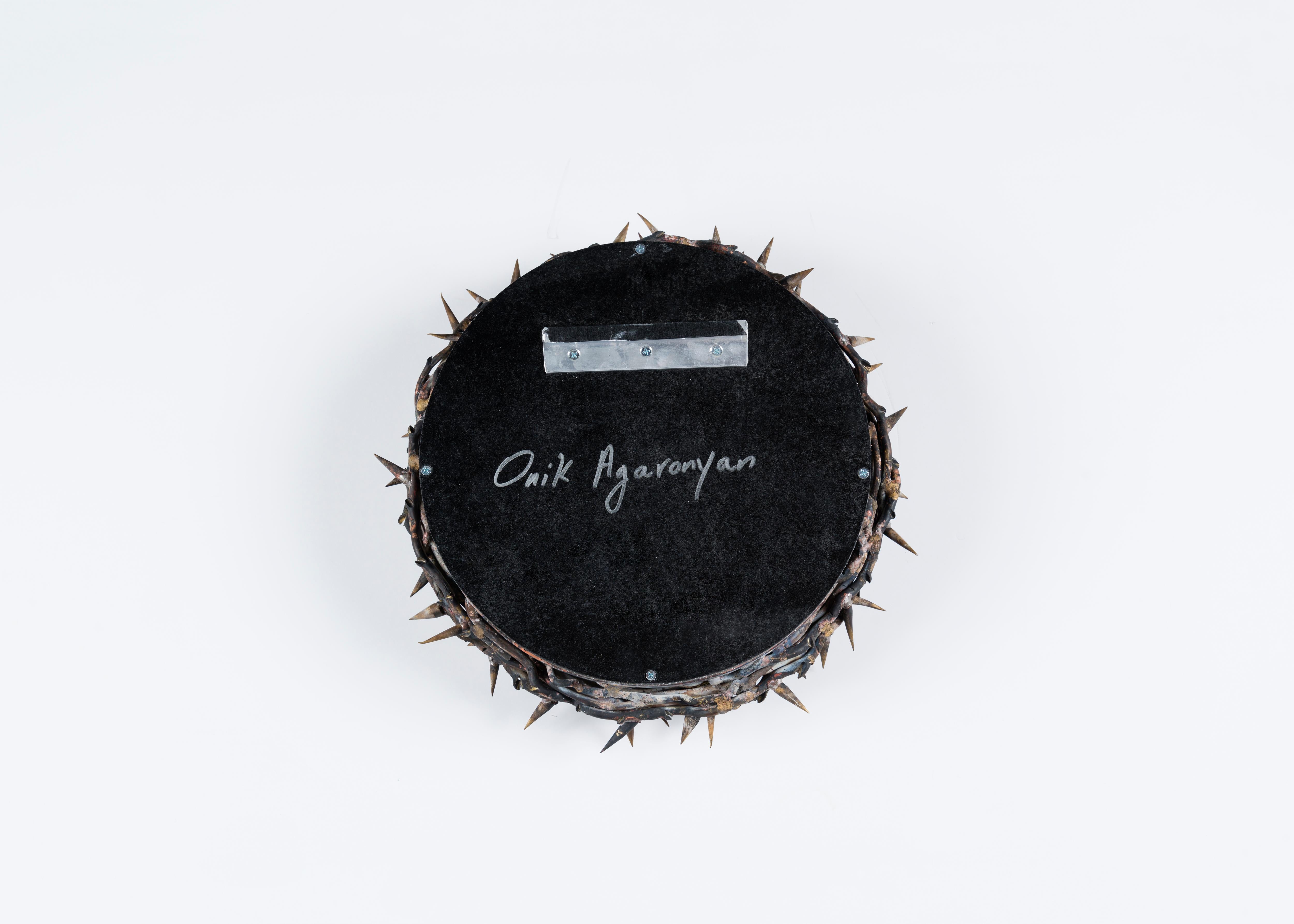 Signé : Onik Agaronyan

Ce miroir sculptural, avec son cadre en laiton et en cuivre brut, évoque la brutalité de la couronne d'épines portée lors de la crucifixion. Reflétées dans le miroir au centre, les épines semblent même se multiplier.