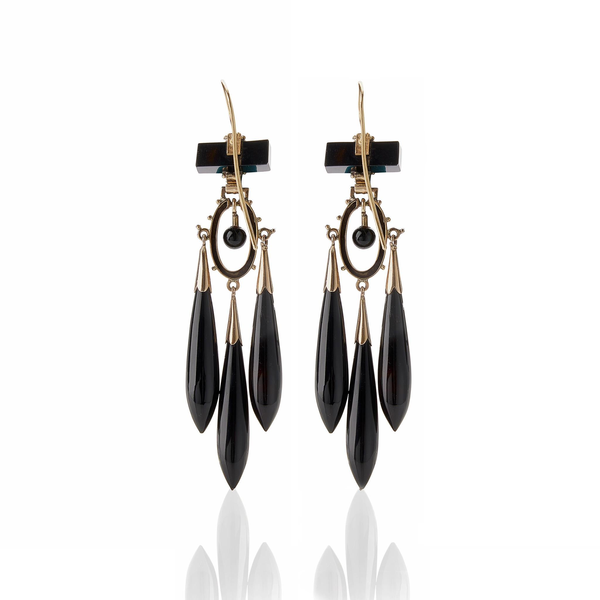 Composed of onyx, enamel and 14K gold, these antique pendant earrings were created around 1870. Each is designed as an onyx bar suspending a cascade of flexibly-set sphere, black enamel oval element and three tapering onyx drops with shaped enamel