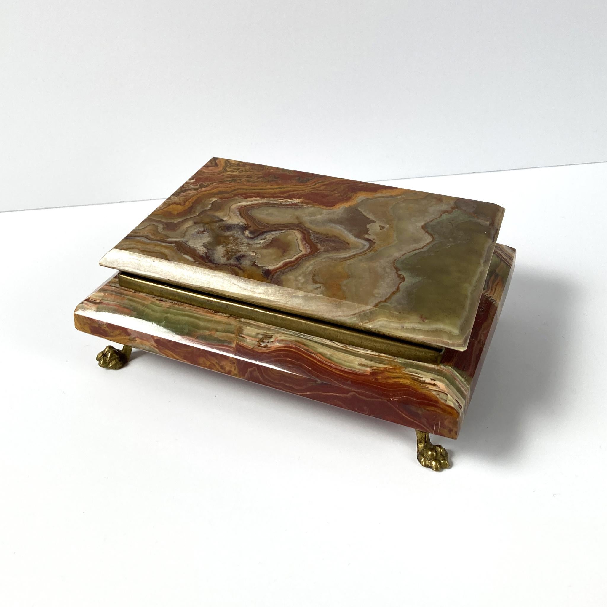 Stunning onyx marble box with brass hinged lid and charming brass feet. Lined with red velvet, which shows a black mark on the interior. The marble exhibits  swirls of brown, taupe, amber and red at every angle. In good vintage condition, no chips