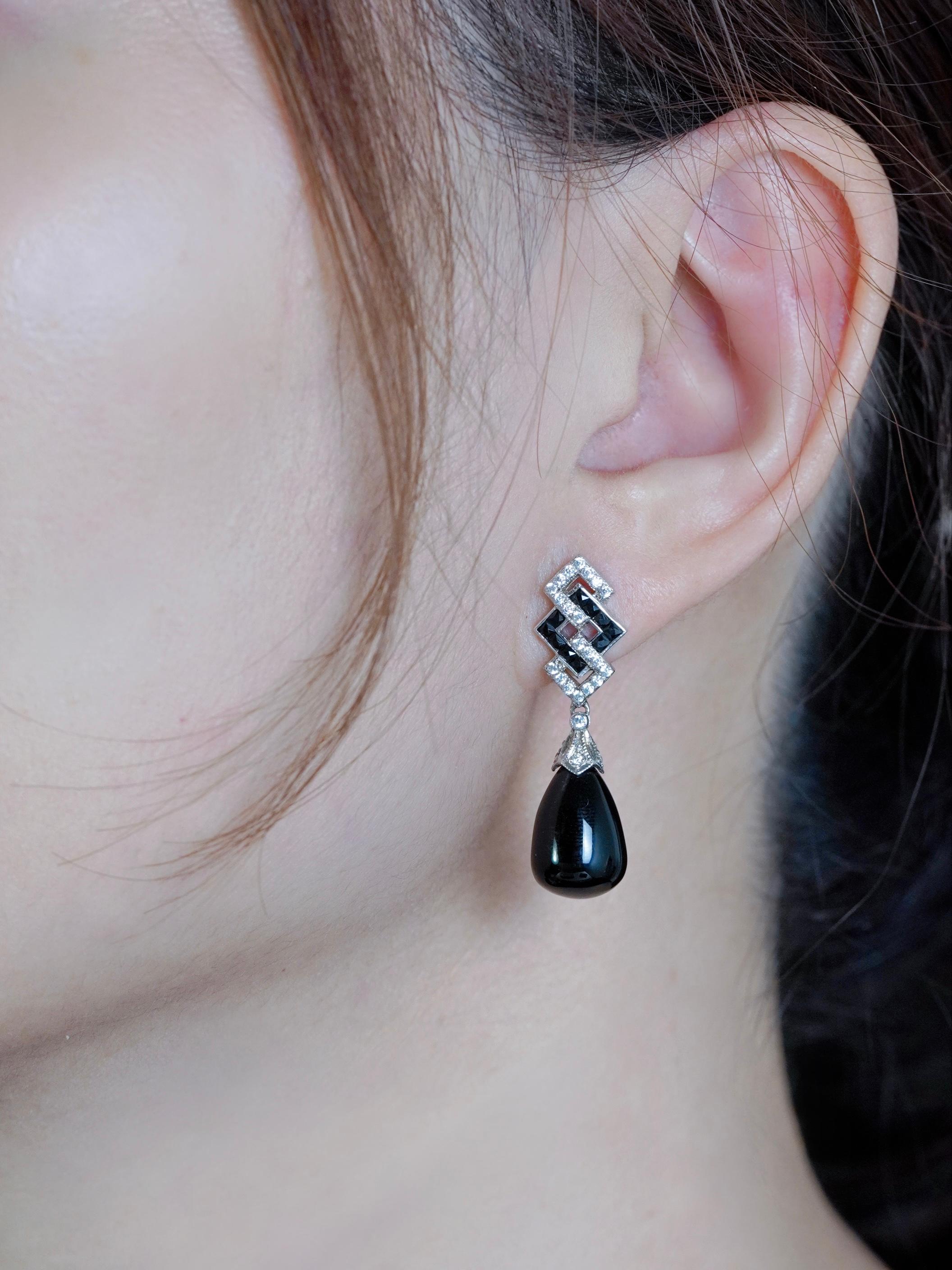 Featuring sleek black onyx elements contrasted by sparkling white diamonds, the design showcases the striking geometric patterns iconic to the Art Deco era. The graceful drop silhouette adds movement and sophistication, making them perfect for