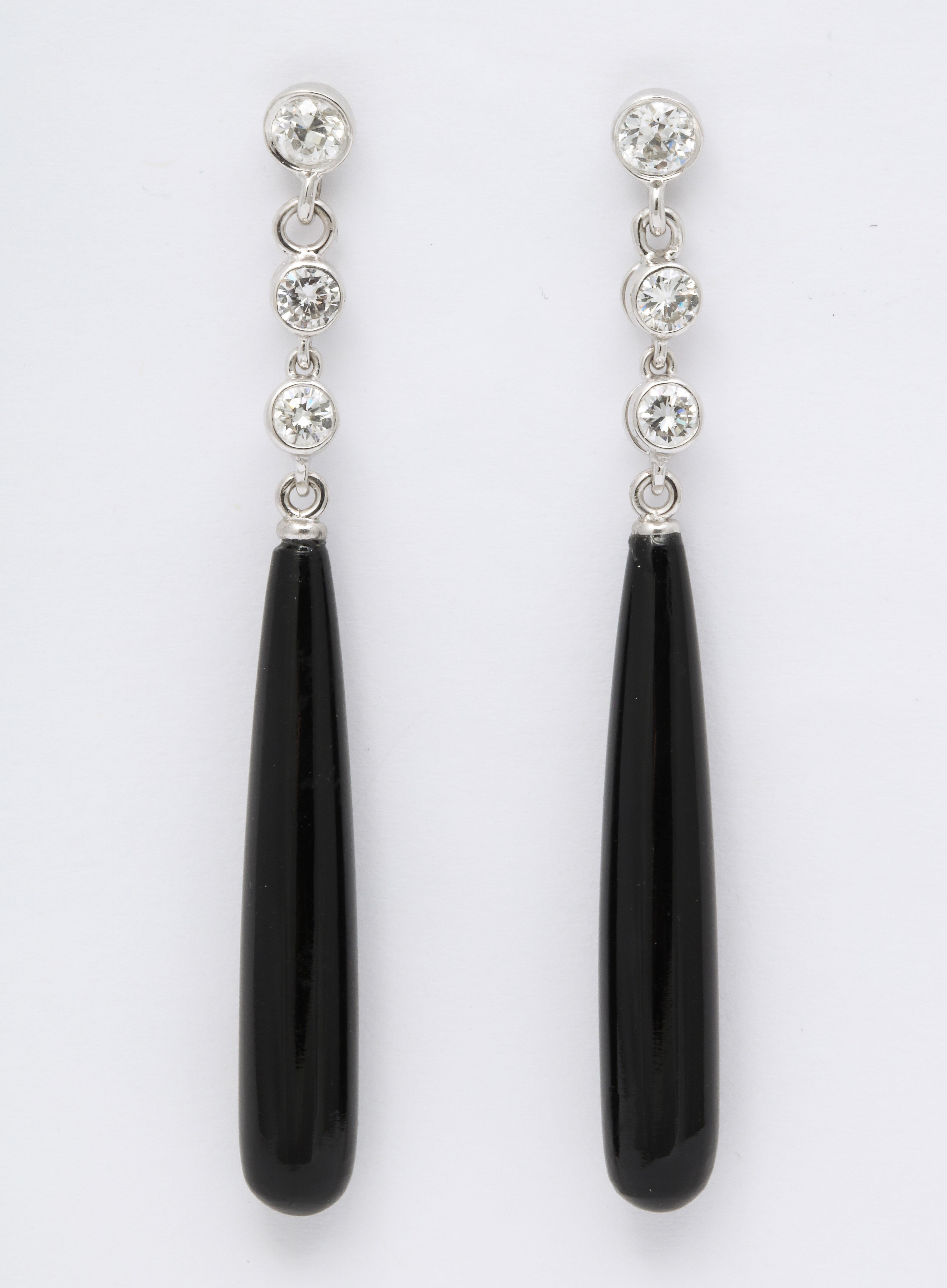 Ces boucles d'oreilles pendantes en onyx et diamants sont de style Art déco classique et peuvent être portées en journée ou en soirée. Ils sont suspendus à trois diamants sertis en biseau et sont conçus de manière à ce que le pendentif en onyx