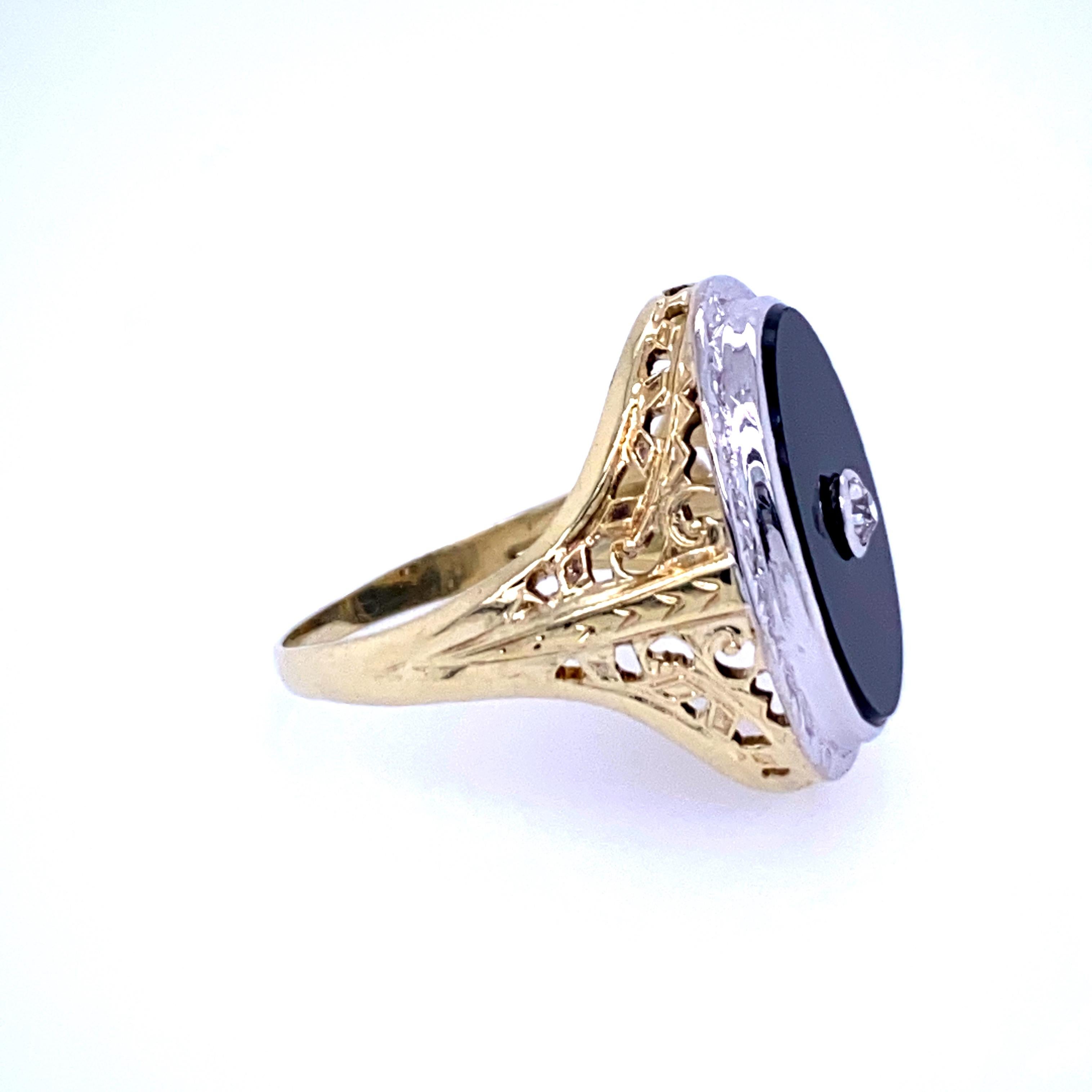 One 14 karat yellow and white gold (stamped 14KT) ring set with one 16.6 x 12.2mm oval onyx in a white gold bezel with one center bezel set Old Mine cut diamond approximately 0.06 carat. The yellow gold filigree shank measures 5.2mm near the top of