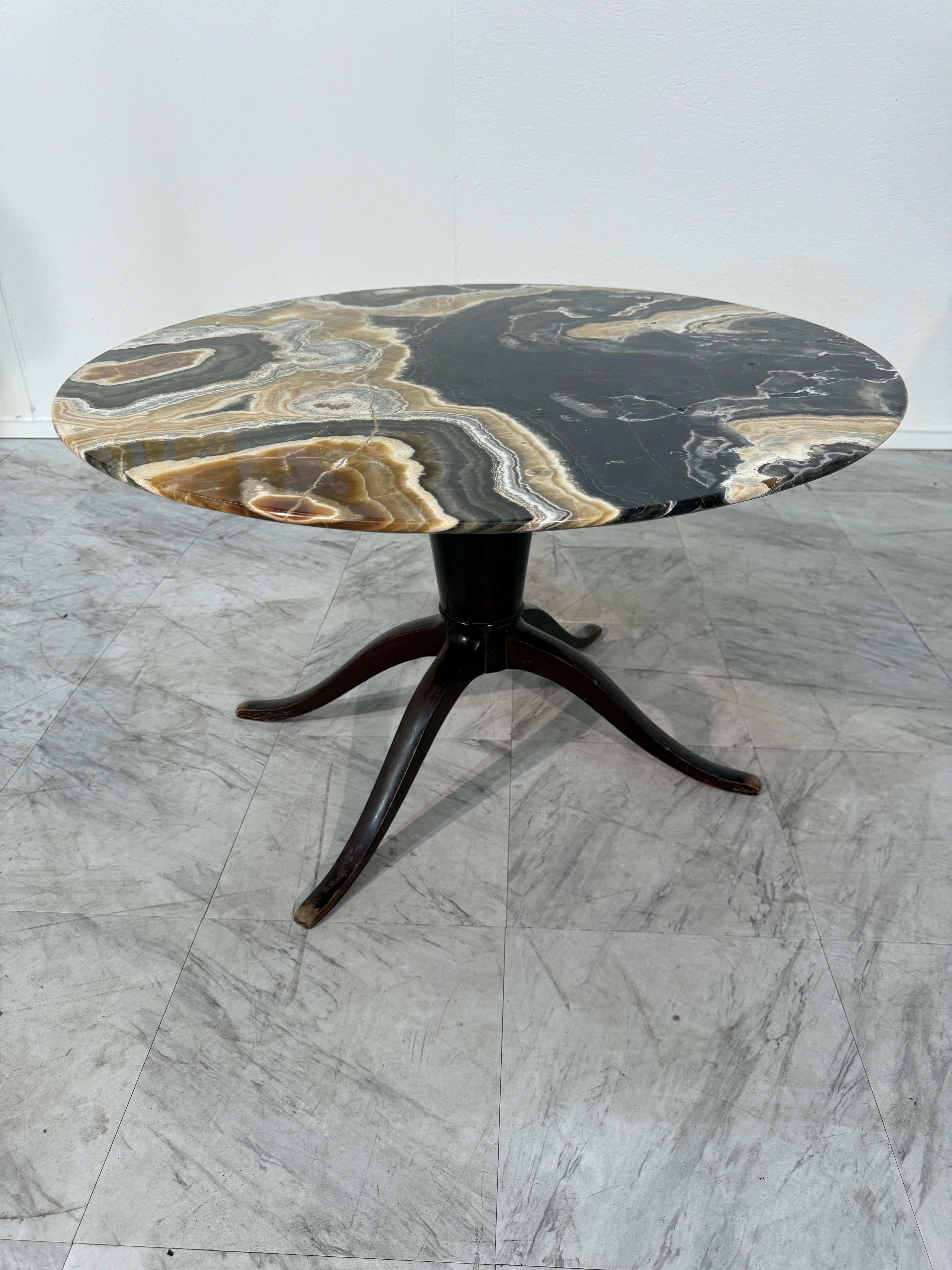 A symphony in stone, this vintage Italian table captivates with its round onyx top, where rich veins of black, caramel, ivory, and smoke swirl in mesmerizing natural patterns. Each striation appears like a deliberate stroke of earth’s own artistry,