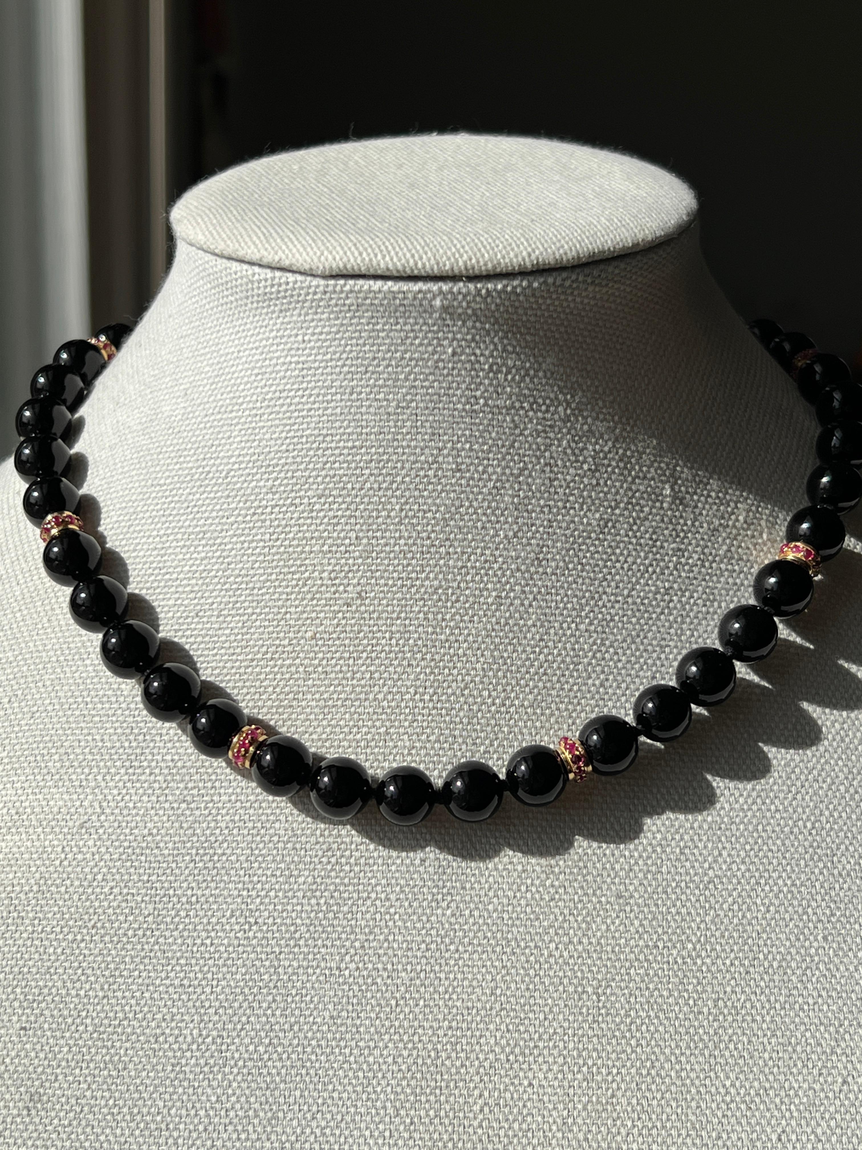 This striking 18 karat yellow gold onyx, ruby, and white jade necklace offers bold gemstone beauty and luxurious craftsmanship, showcasing rich black onyx, vibrant natural rubies, and a substantial white jade clasp element. The elegant 17.5-inch