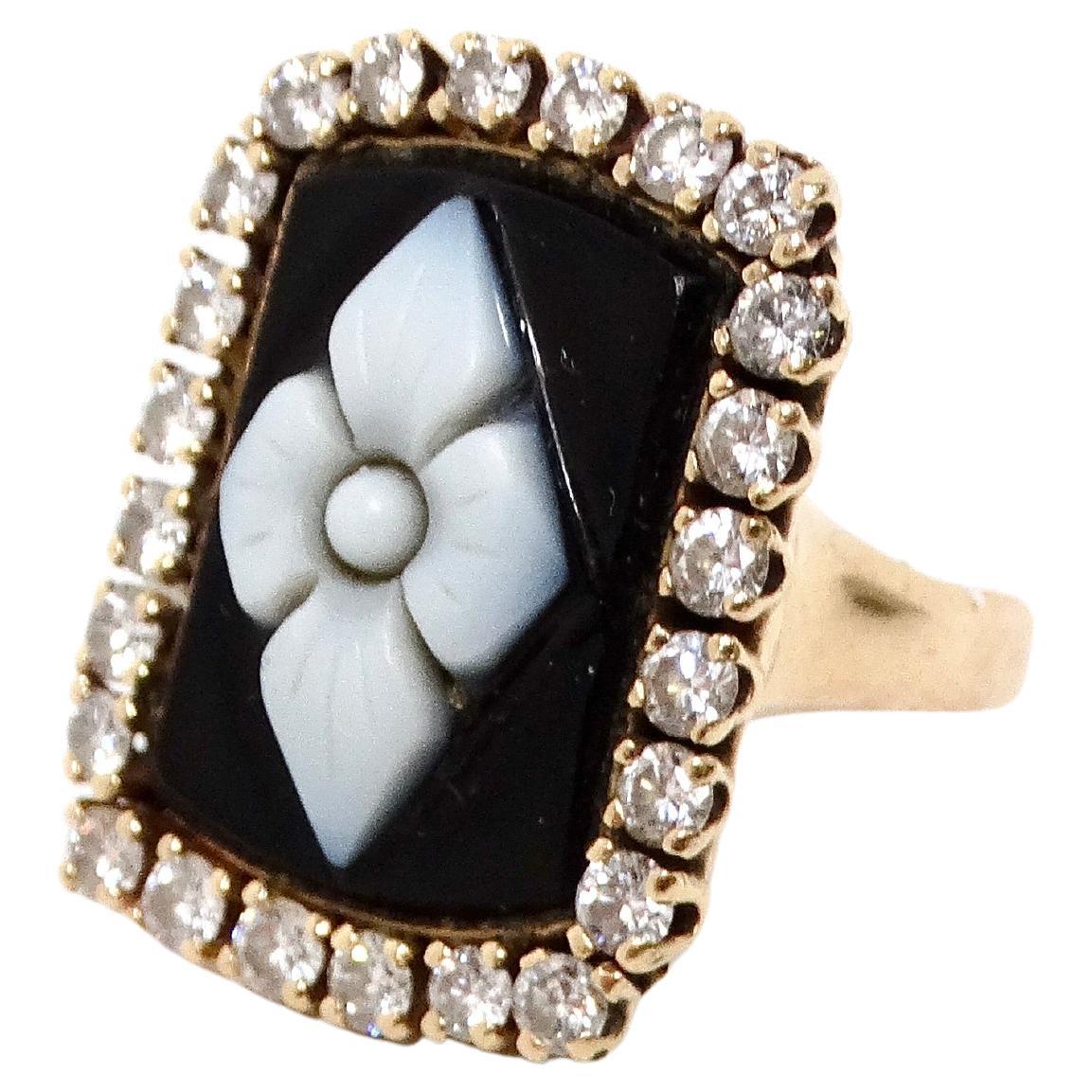 The Onyx Flower Motif Diamond Set 14k Yellow Gold Cocktail Ring is a stunning statement piece that exemplifies elegance and craftsmanship. The ring features a striking rectangular onyx stone, meticulously cut and carved to measure 18mm by 11mm, with