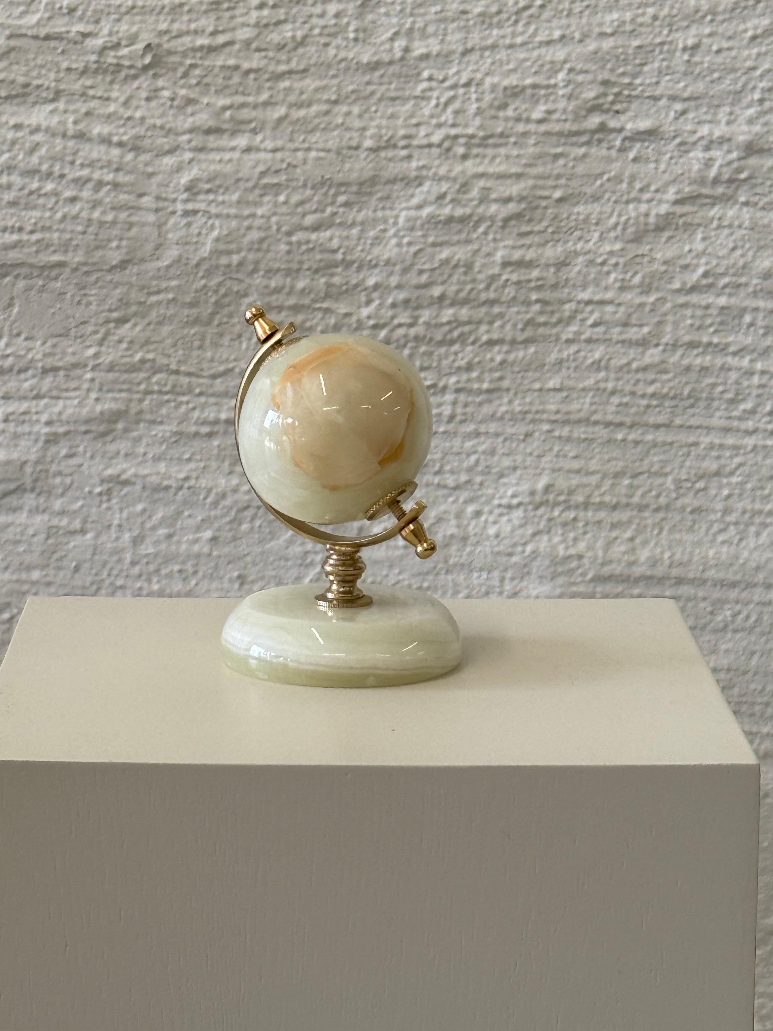 Rehaussez votre bureau avec ce presse-papier globe en onyx magnifiquement travaillé. Dotée d'une sphère en pierre polie aux teintes naturelles beige et crème, elle est montée sur un socle robuste avec des accents en métal de couleur dorée. Parfait