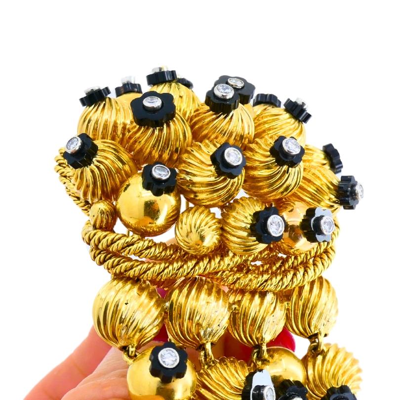 A whimsical black onyx and gold bead brooch, circa 1950s.
The brooch is designed as a cluster of rounded gold beads, alternating in size and texture, which gives the pin a great dynamic quality. Some of the beads are smooth, while others have a