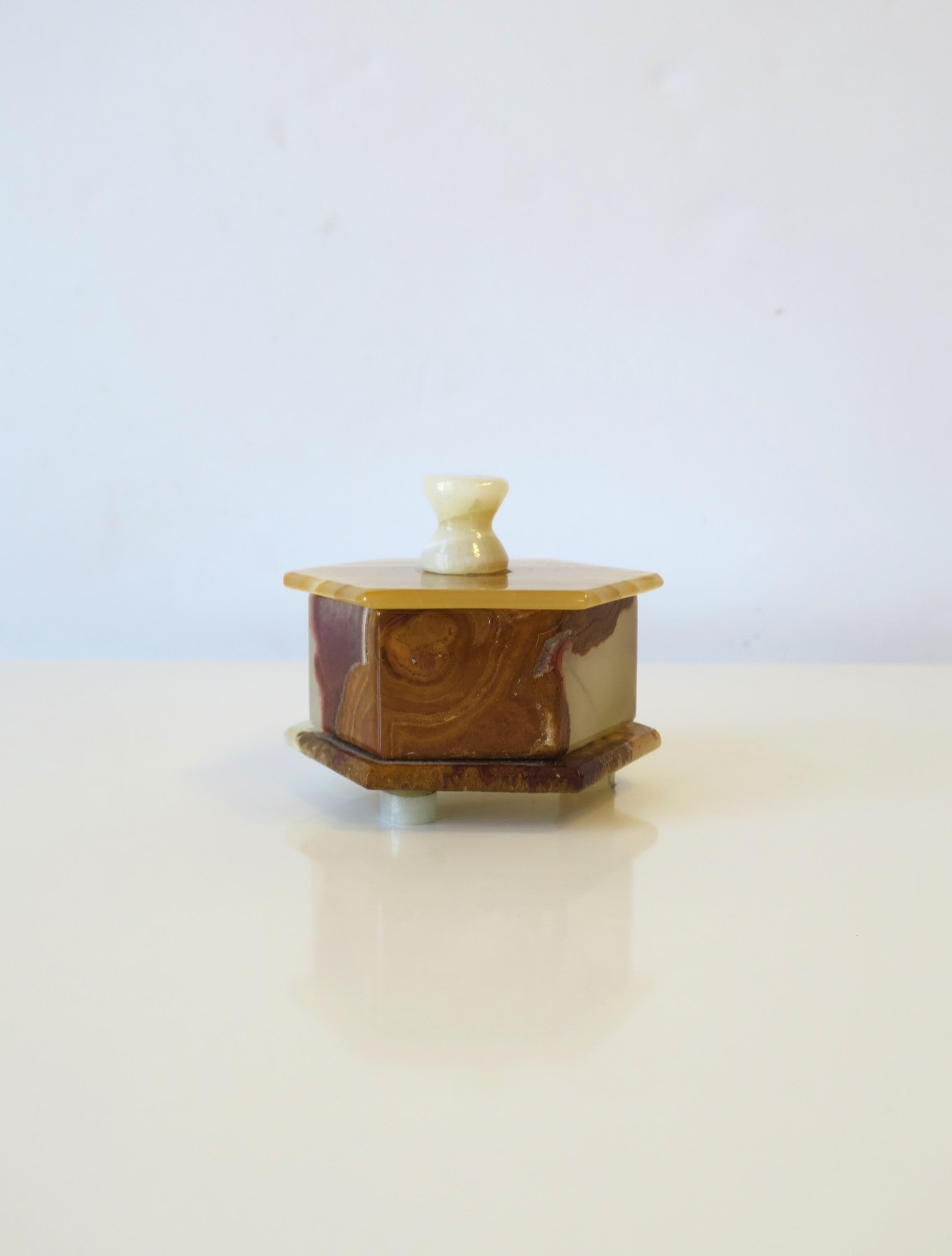 A small '70s modern hexagon shaped onyx box with lid, circa 1970s. Box is multicolored onyx, in a hexagon shape with lid and feet. A nice piece to hold small items on a desk, or small jewelry on a vanity, etc. Dimensions: 3.38