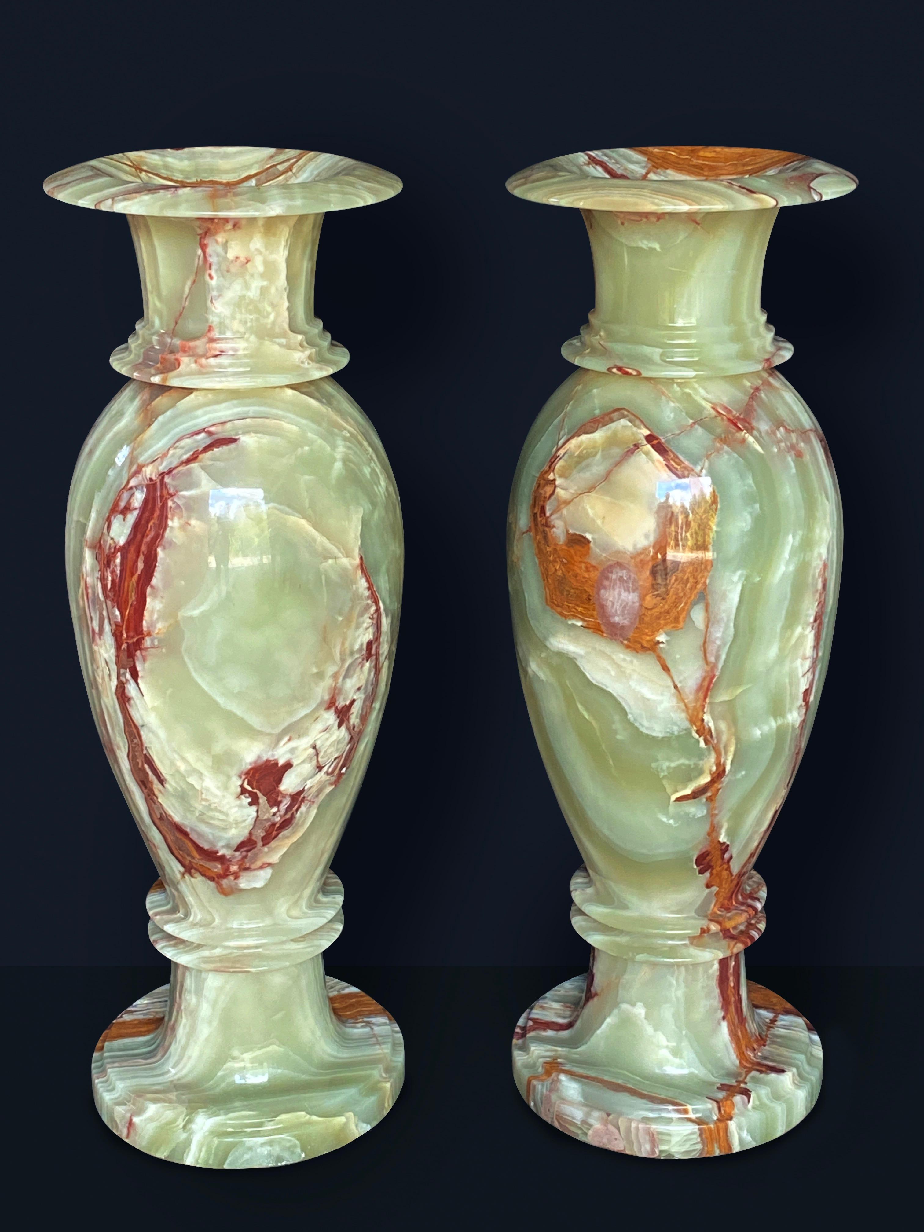 Life-size pair of green and red onyx turned polished vases, the rolling rims above slender baluster form terminating in circular bases. The onyx vases are carved from single blocks of highly figured onyx marble. Primarily rich green emerald colors