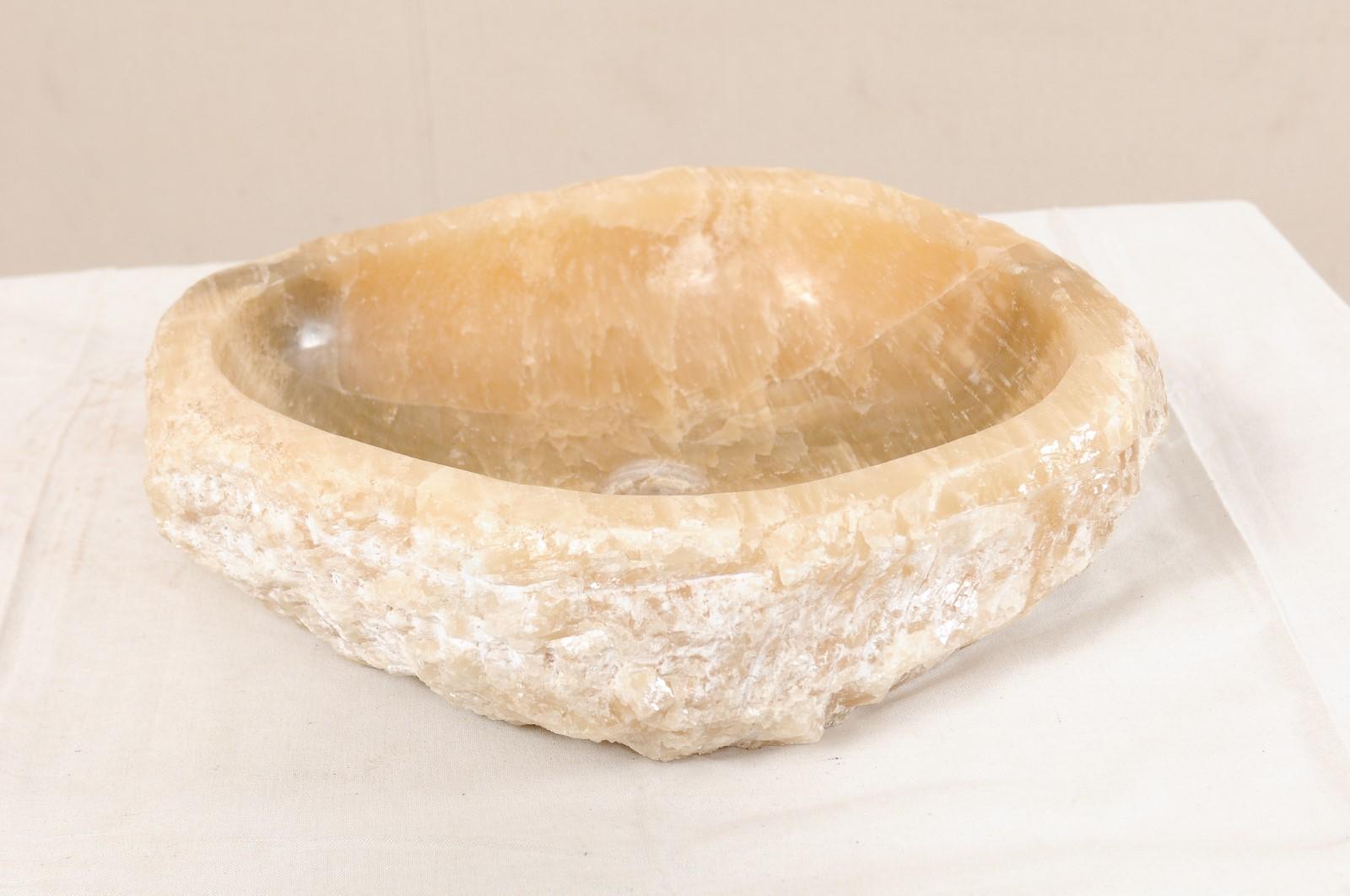 Une vasque en onyx naturel avec bord vif d'origine. Cet évier sculpté, créé à partir d'une roche brute d'onyx, est doté d'un bassin intérieur sculpté puis poli, ce qui facilite le nettoyage. La pierre texturée naturelle reste sur l'extérieur de