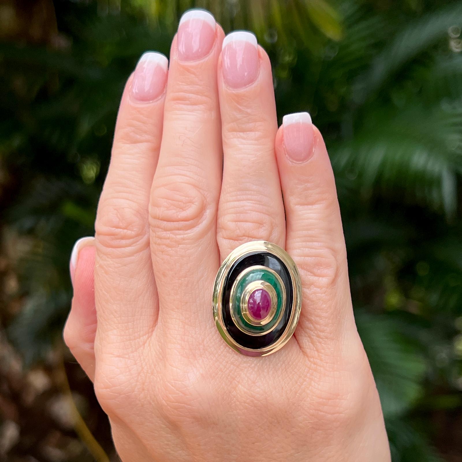 Contemporary late twentieth century onyx, ruby, and enamel cocktail ring crafted in 14 karat yellow gold. The oval vintage ring features cabochon black onyx, green enamel, inlay, and a cabochon red ruby gemstone. The oval top measures 22 x 30mm, and