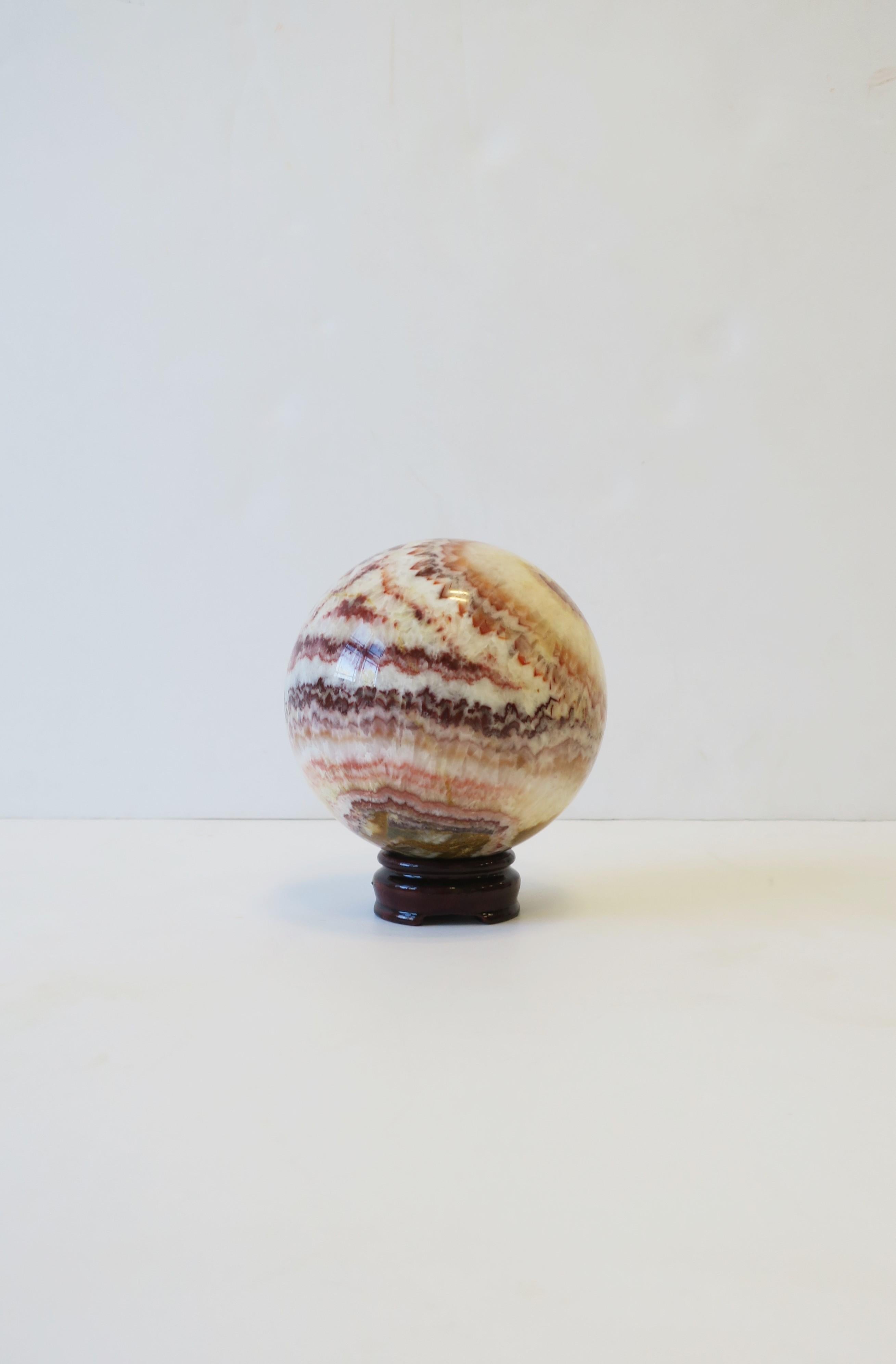 A beautiful and substantial vintage '70s Modern onyx marble sphere decorative object with wood stand, circa 1970s, late-20th century, Italy. Predominant colors hues include white, light red, red burgundy, with touches of yellow mustard.