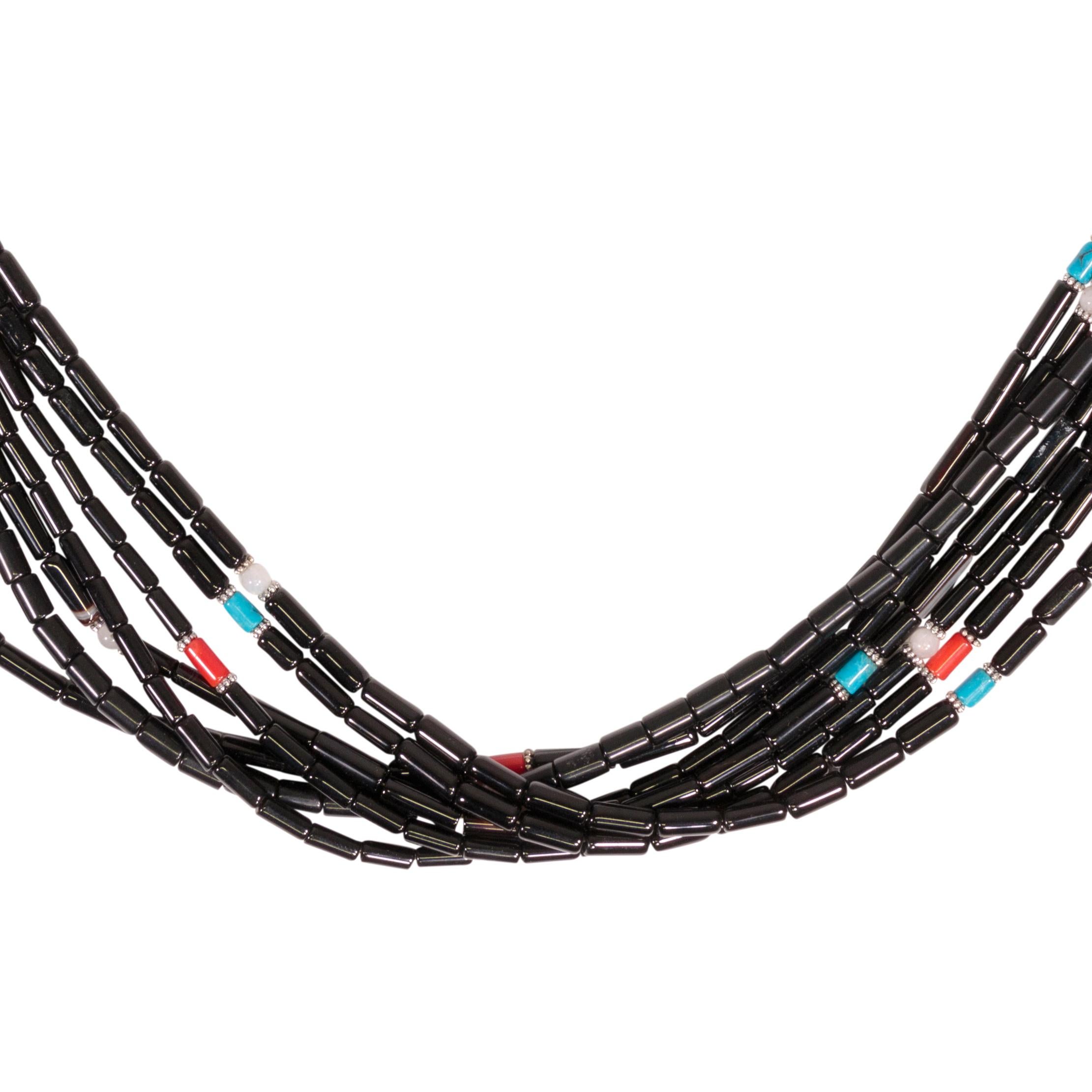 Collana a più fili firmata da Tommy Singer. Perline tubolari in onice con accenti in argento e oro 14k, turchese, turchese e corallo. 

Tommy Singer (1940 - 31 maggio 2014) è stato un argentiere navajo di fama mondiale e il suo stile distinto di
