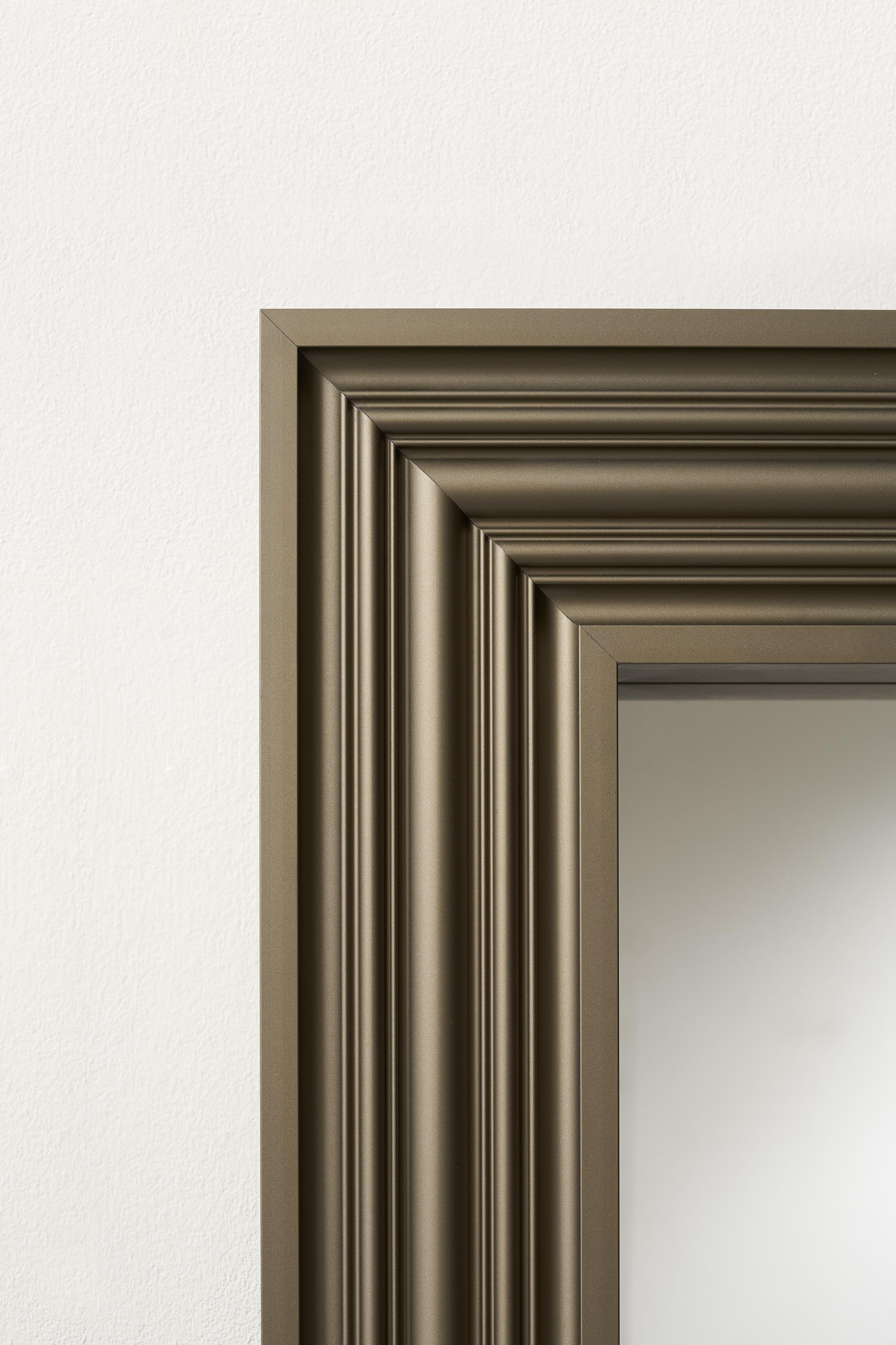 Floor mirror with frame in anodized extruded aluminum on three sides. 
The mirror is fixed onto a panel that ensures safety and stability.
It requires floor support and wall fixing.
Finishes: satin-finished burnished brass, satin-finished silver.