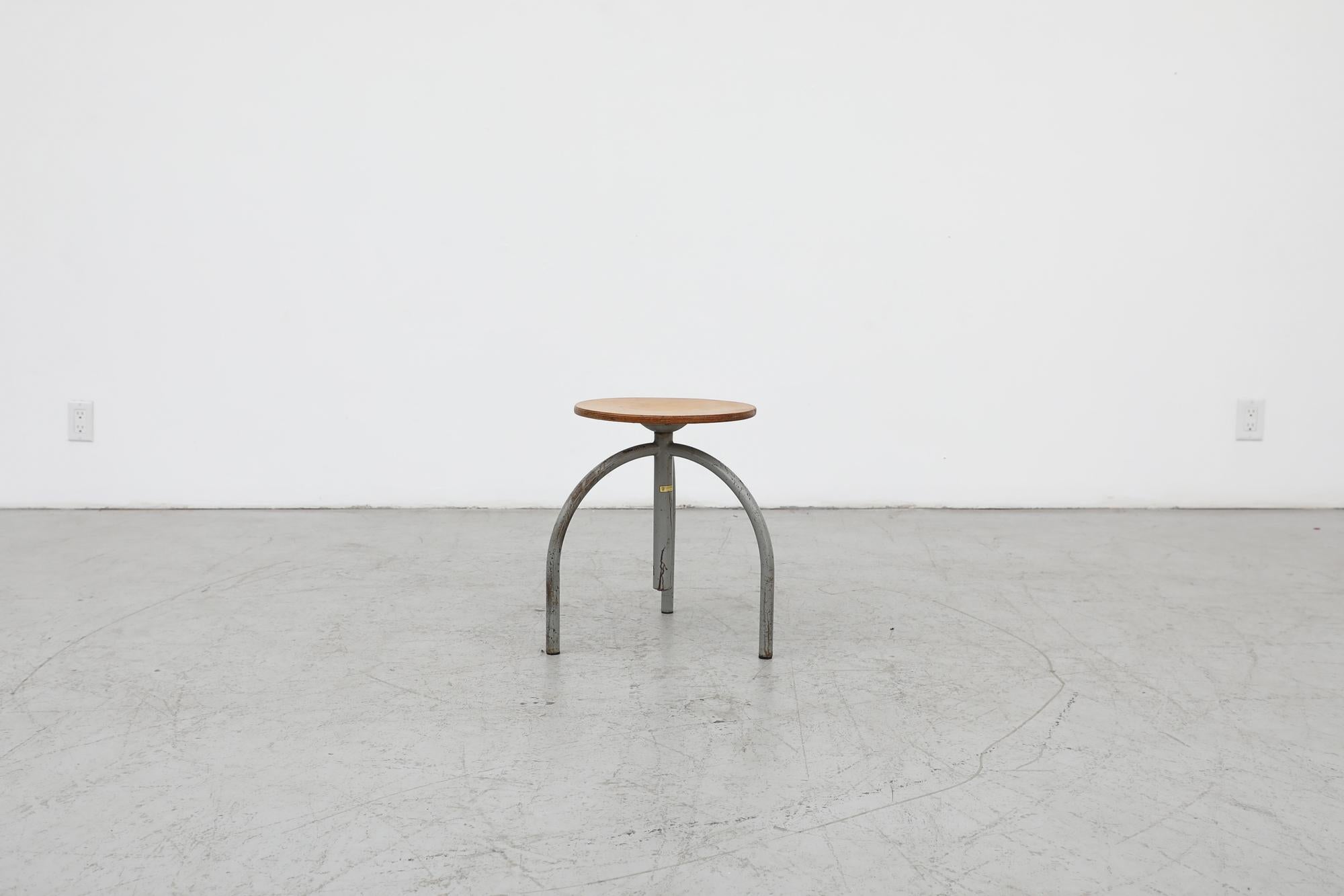 Mid-Century Industrial tripod task stool by Cor Alons for Oosterwolde. The seat is a layered and formed birch plywood on a threaded stem for height adjustment. The frame is made of fat hollow enameled metal tubing. In original condition with visible