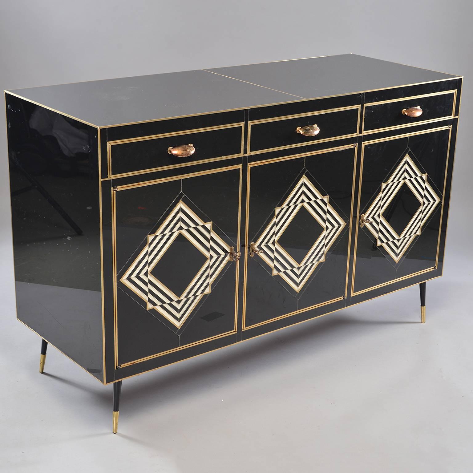 Italian glass clad credenza, sideboard or buffet cabinet, circa 1960s. Underlying cabinet structure is wood and piece is entirely covered (with exception of back and legs) in black and cream colored Murano glass with brass accents. Cabinet consists