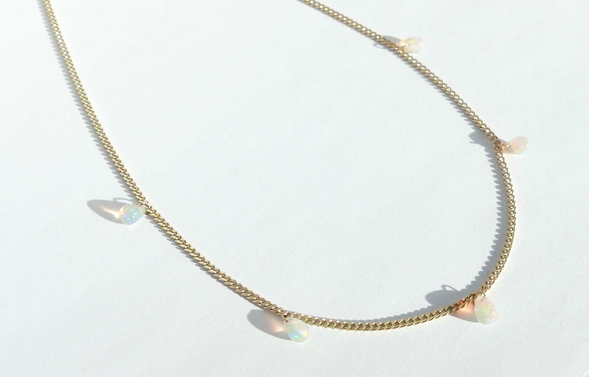 This contemporary necklace features five Ethiopian opal drops dangling from a sleek 18 karat gold curb chain.  Measuring just under 2mm wide, the chain is 16 inches long and is finished with a lobster catch.  The opals display a rainbow-like
