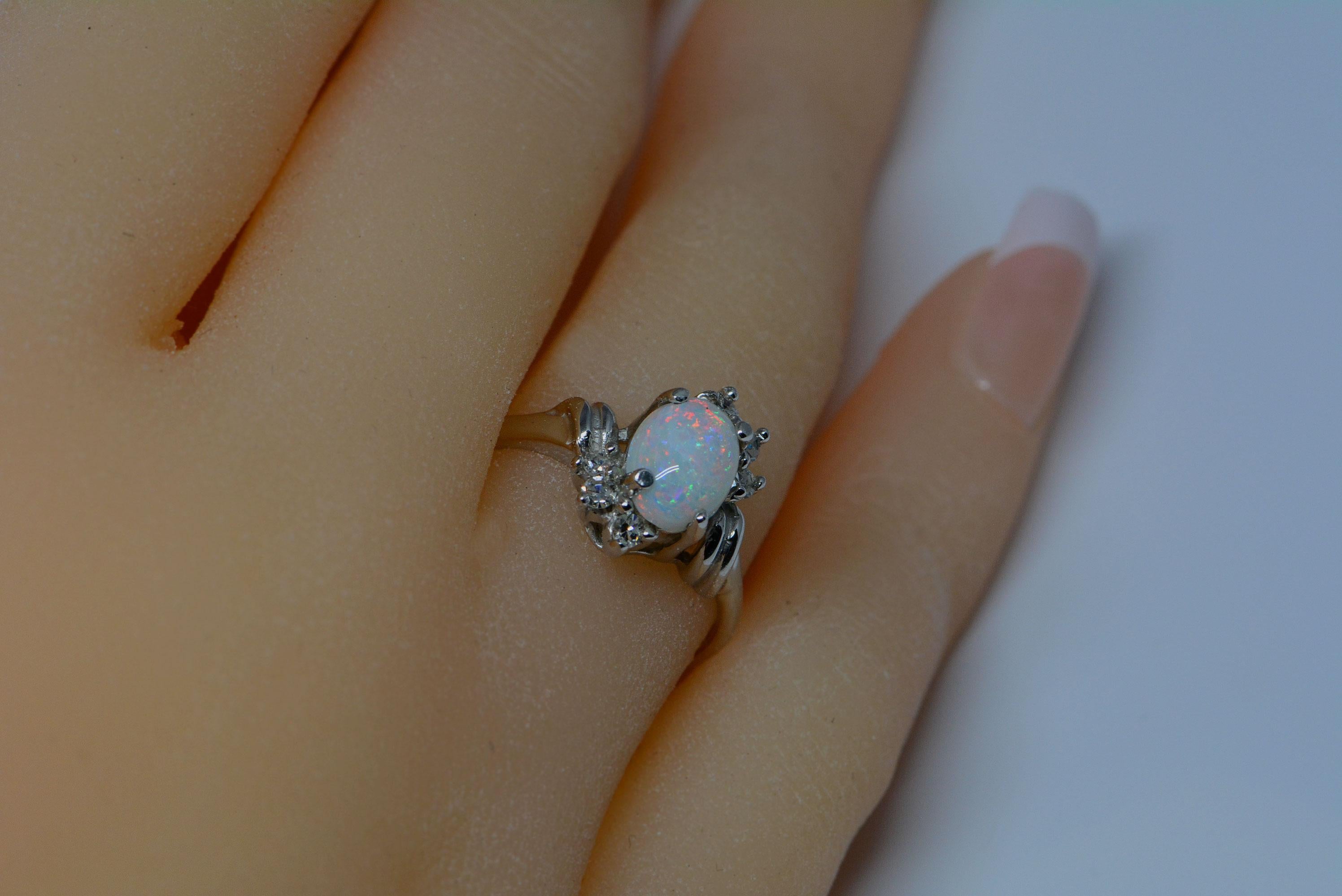 The opal in this ring has a nice play of colour that is accented by a 10 karat white gold band. The opal weighs: 0.80ct and is an oval cabochon cut. 
This ring has six single cut diamonds surrounding the opal that weigh: 0.14ctw, and are Vs1