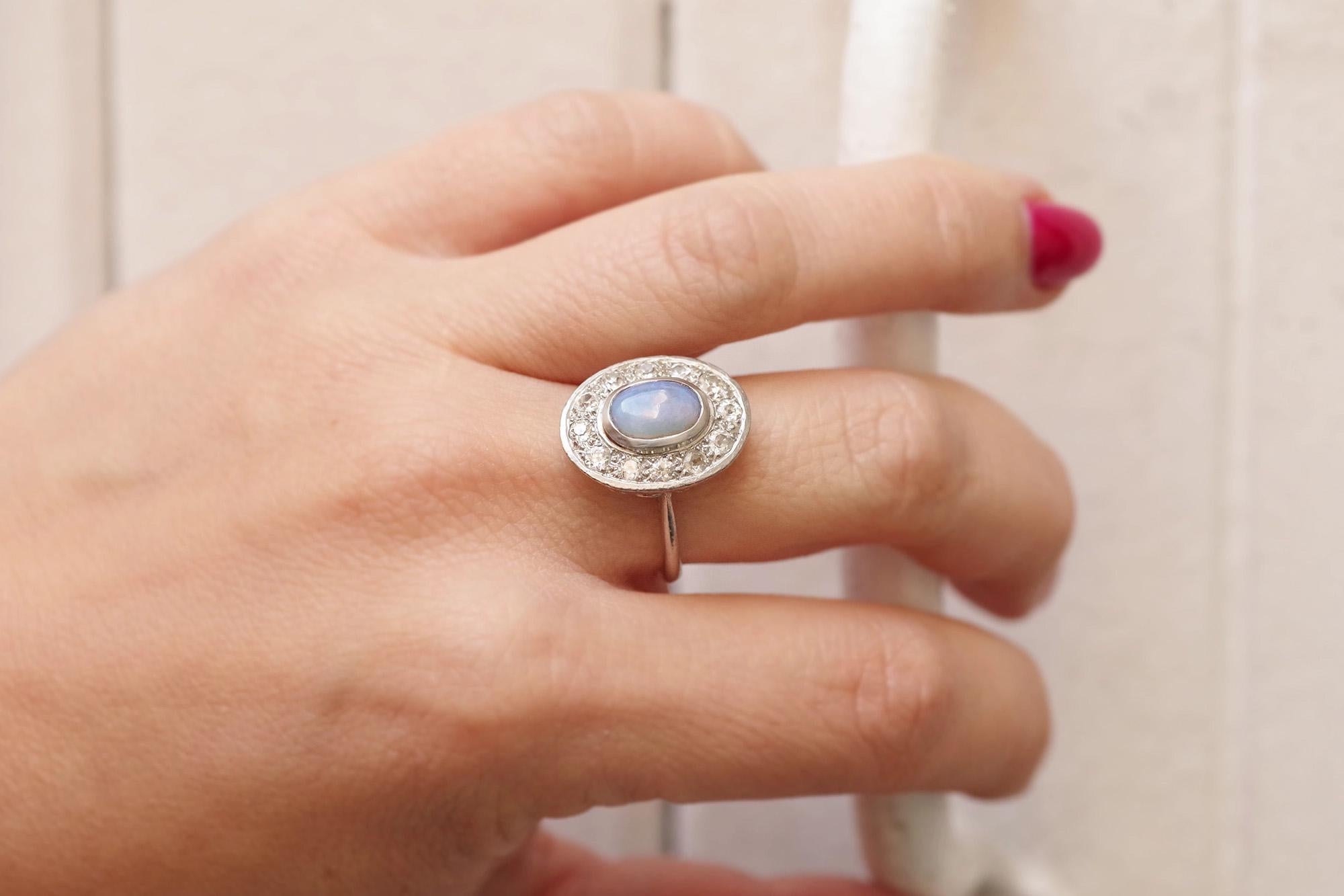 Anello Art Deco con opale a grappolo in platino. Questo antico anello a grappolo presenta un opale centrale con taglio cabochon incastonato, circondato da dodici diamanti di vecchio taglio. L'opale mostra vibranti giochi di colore con sfumature di