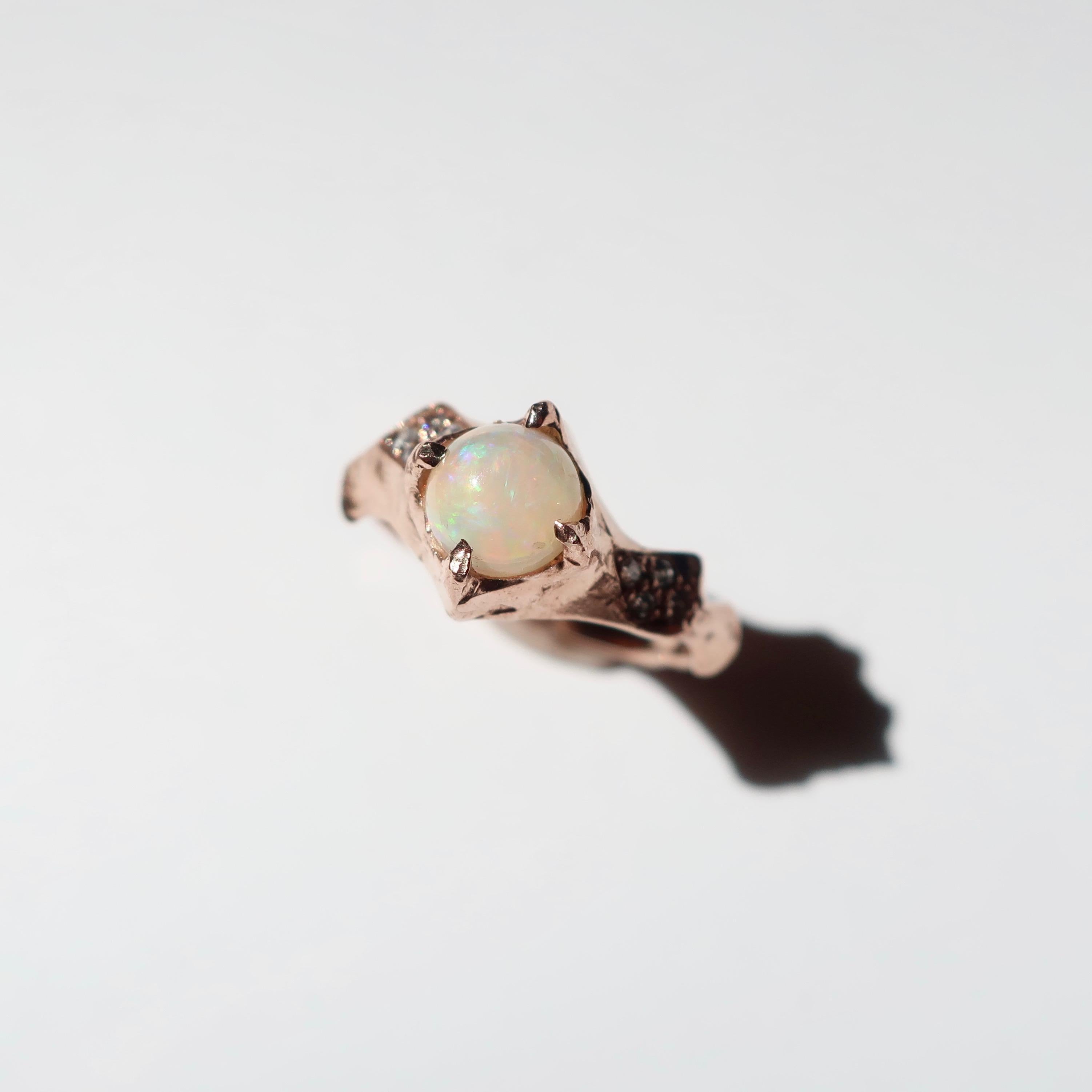 Hand crafted ring in 14K Rose Gold with a clustering of pave white diamonds on either side.  A 6mm opal cabochon is set in the middle that has  beautiful pink and yellow flashes. This piece combines timeless elegance with the signature hand texture
