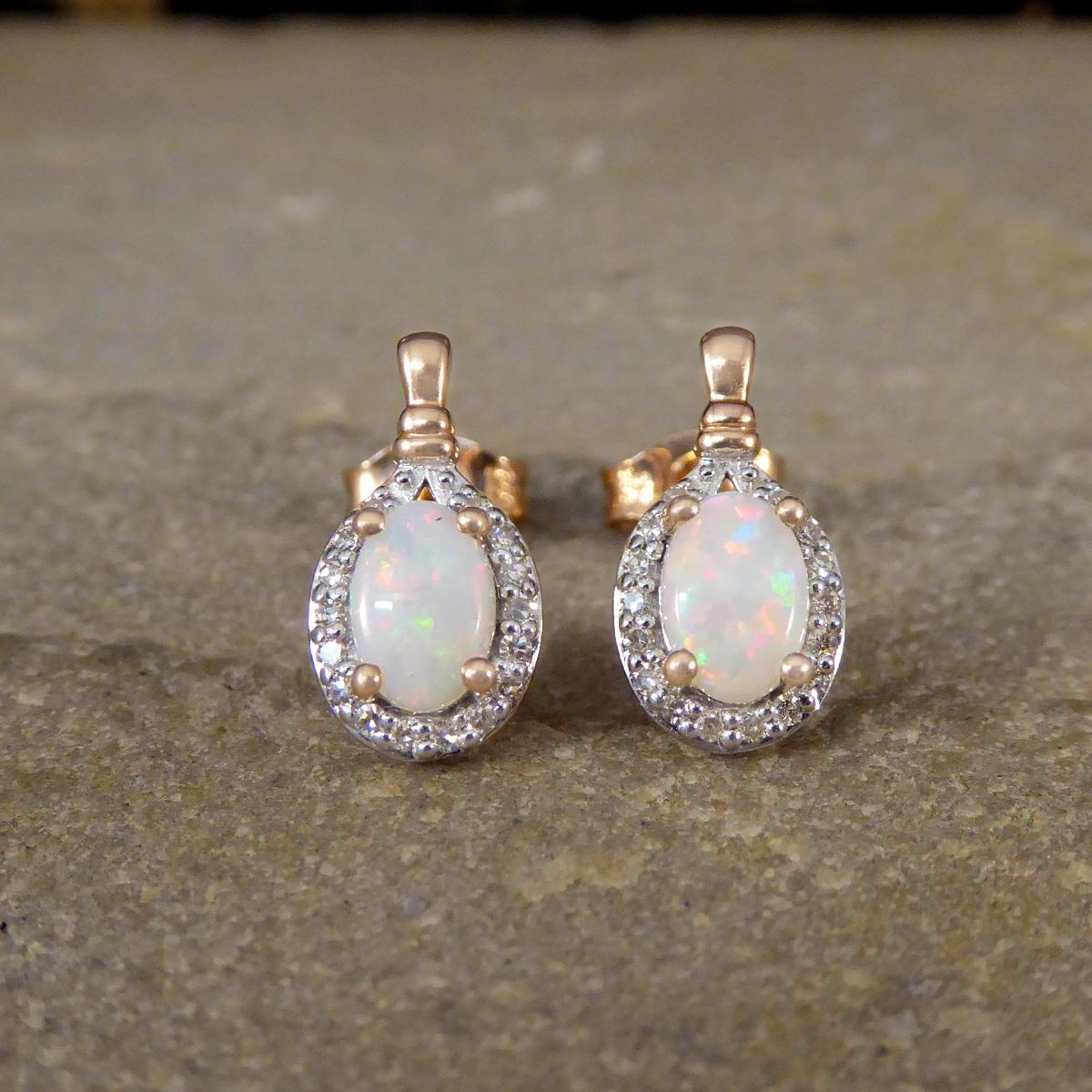 A lovely pair of Opal and Diamond drop earrings. Featuring in each earring stud are a four claw Rose Gold set light Opal showing a subtle red colour show with slight blue and green flashes. The Opals are surrounded by a cluster of Diamonds weighing