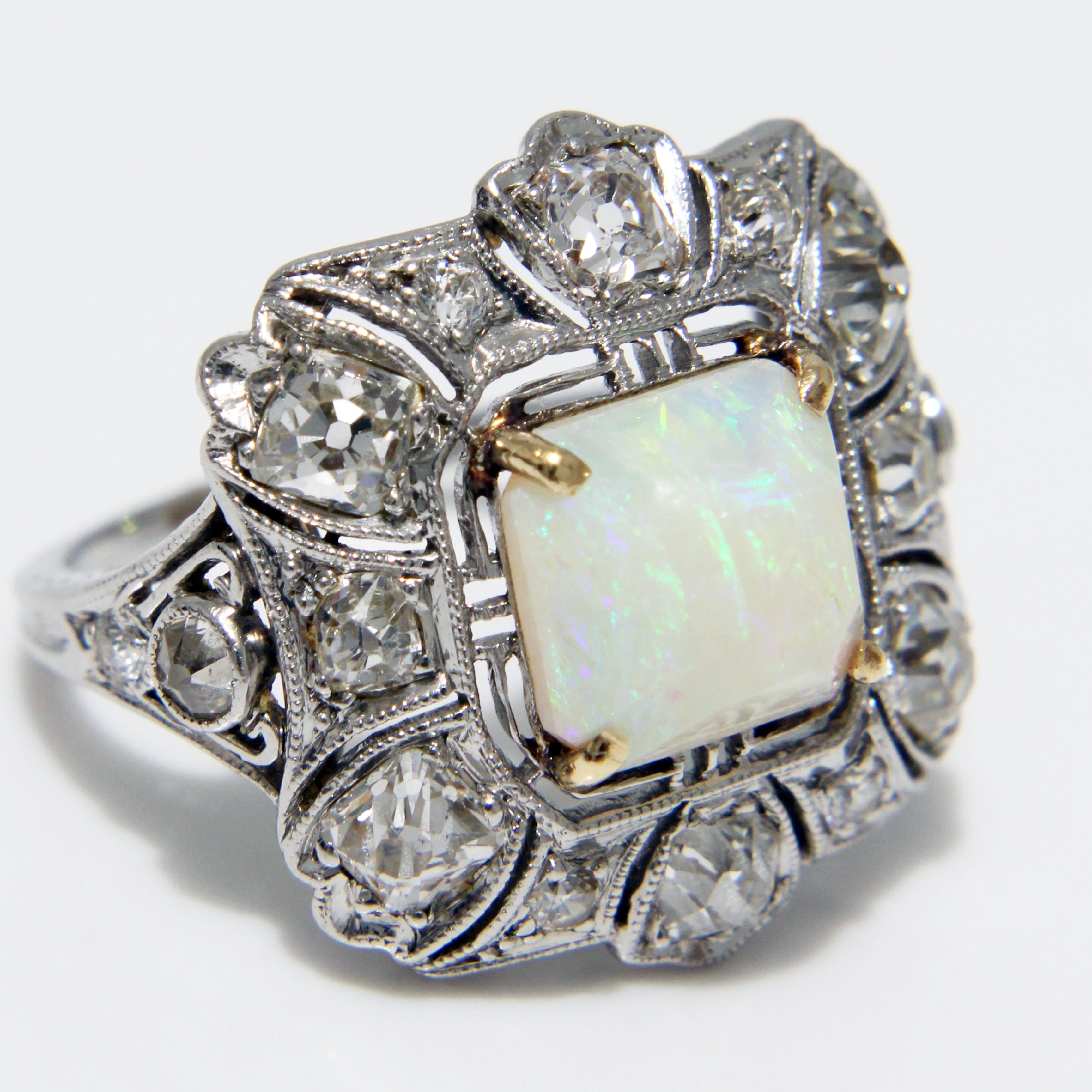 Anillo de cóctel de ópalo y diamantes de estilo Art Decó de segunda mano, probablemente fabricado a principios del siglo XX.  Realizado con un engaste de platino, presenta un gran ópalo cuadrado rodeado de 16 diamantes redondos.  Una pieza de alta