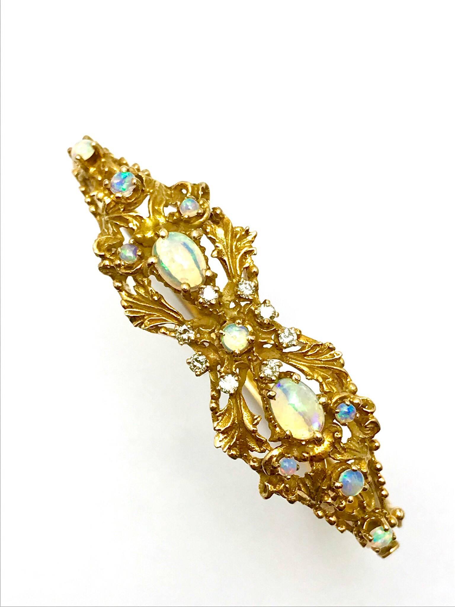An opal and diamond 14 karat yellow gold bangle bracelet.  The bracelet is hand crafted with eight diamond surrounding the center opal, and five more opals on both sides, set in a detailed foliage design.  The bangle has a hinge and clasp.  Signed