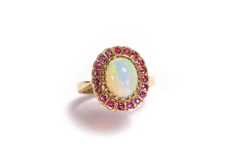 Opal and garnet cluster ring in rose gold 18 karats. A cabochon opal is set with 19 claws. This noble opal presents beautiful plays of color, from bright and luminous yellow, orange, to green, blue and purple. The opal is surrounded by 19 pink