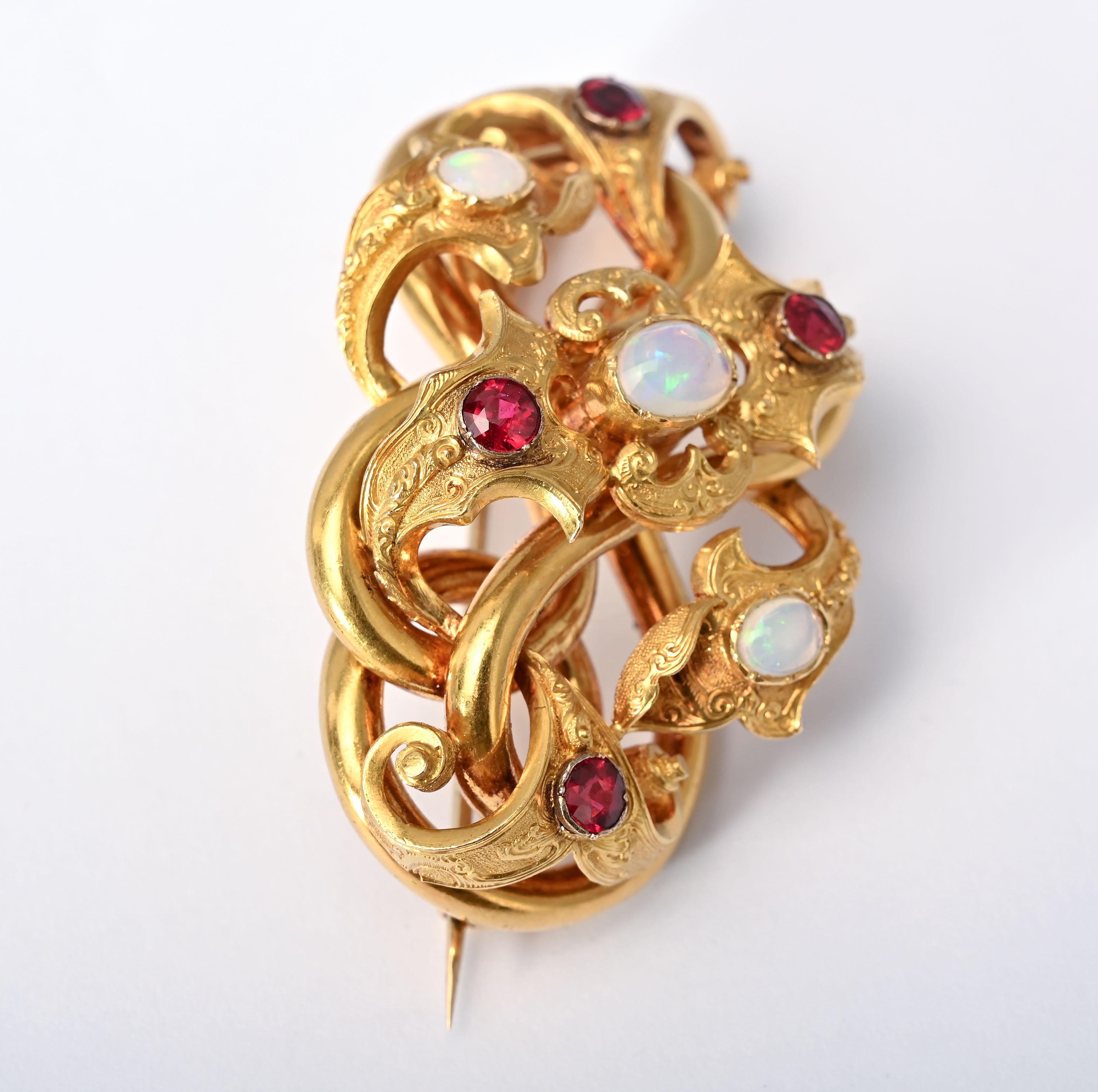 Elegant and unusual gold brooch with  a twisting in and out tubular design. The  brooch has three opals and four garnets mounted on different levels. The brooch is 2 3/8 inches w ide and 1 1/2  inches tall. It is 1 inch from the pinstem  to the top