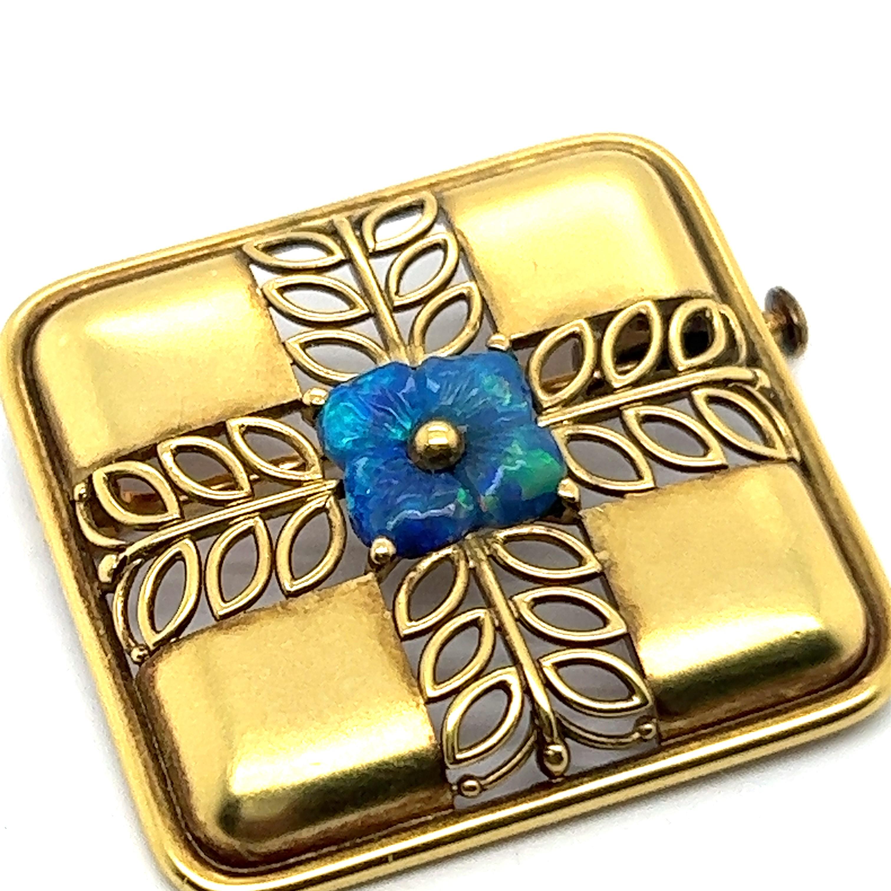 This exquisite vintage opal brooch in 18 Karat yellow gold enchants with elegance. 

At the center of the square design is a small blue opal flower radiating delicate charm. Around the flower is a finely woven pattern that in a cross form. The