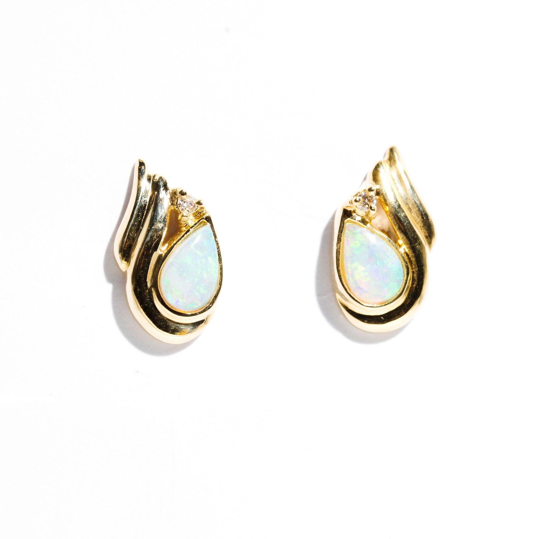 Carefully crafted in 18 carat yellow gold is this delightful vintage pair of stud earrings featuring two oval pear shaped cabochon opals displaying yellow, green, violet and blue play of colour. The opals are each accented with a single round