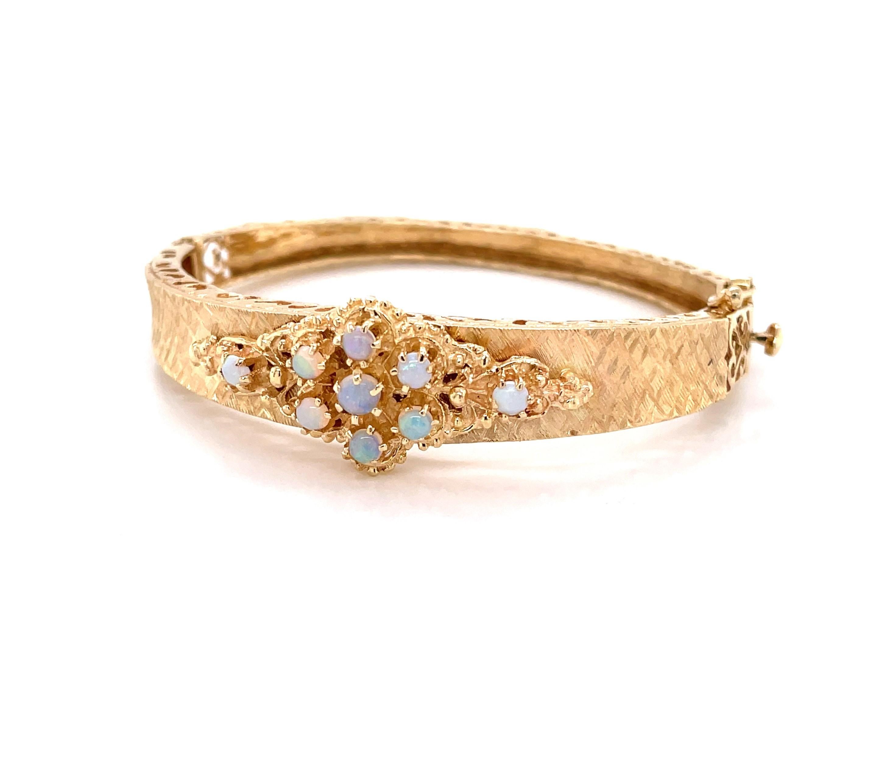 The iridescent natural opal cabochon cluster arranged at the front placket of this unique fourteen karat 14K yellow gold bangle bracelet gives this beautiful piece a regal feel. With filigree side appointments, the textured gold tapers to the back