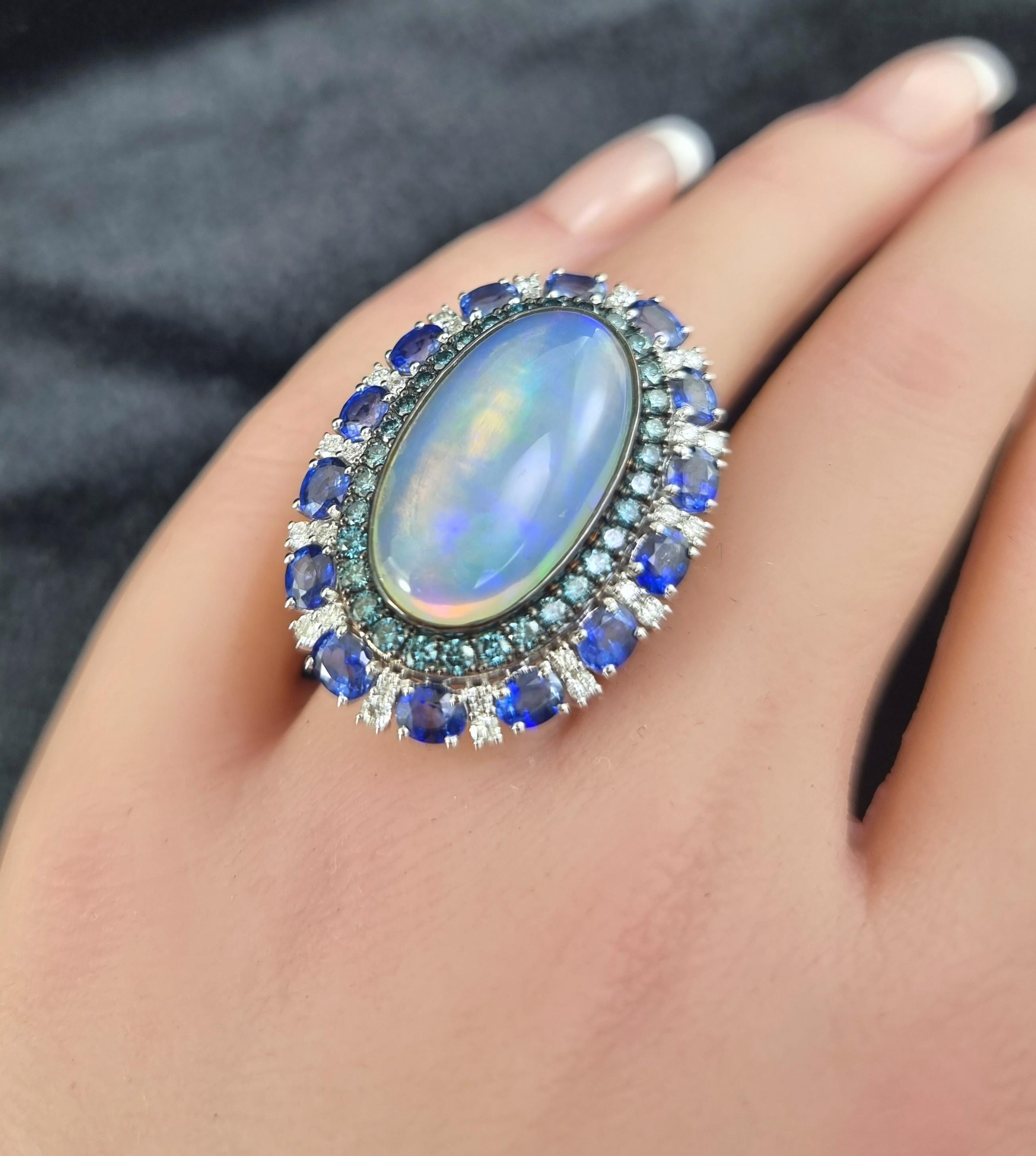 Ein faszinierender Tanz der Farben und des Glanzes: Dieser exquisite Ring zeigt in seiner Mitte einen leuchtenden Opal mit einem Gewicht von 8,56 Karat, der mit schillerndem Feuer strahlt. Ein Halo aus tiefblauen Saphiren (4,64 ct.) und schillernden