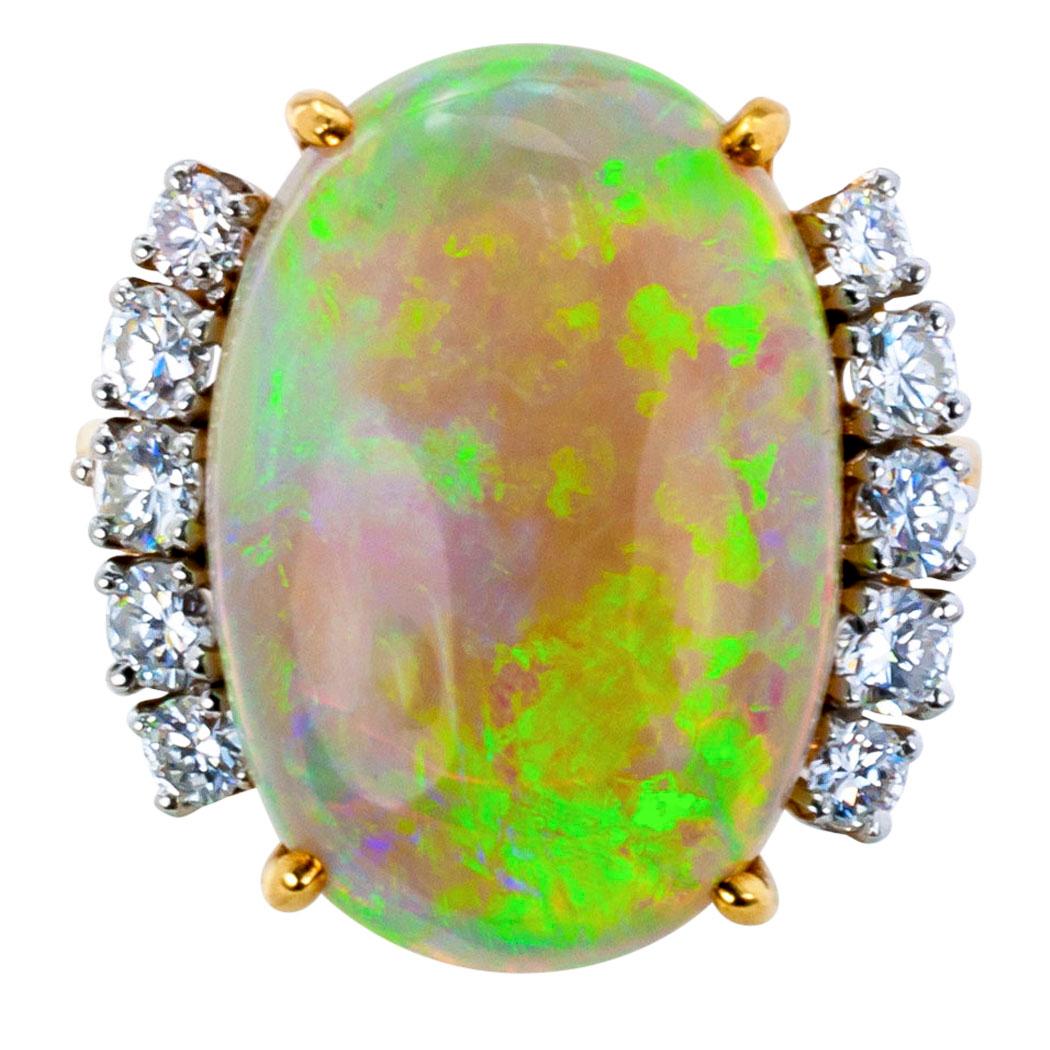 Estate 1970s opal and diamond gold ring. The design showcases an impressive oval opal weighing approximately 9.00 carats, between shoulders set with twelve round brilliant-cut diamonds totaling approximately 1.00 carat, approximately G – H color and