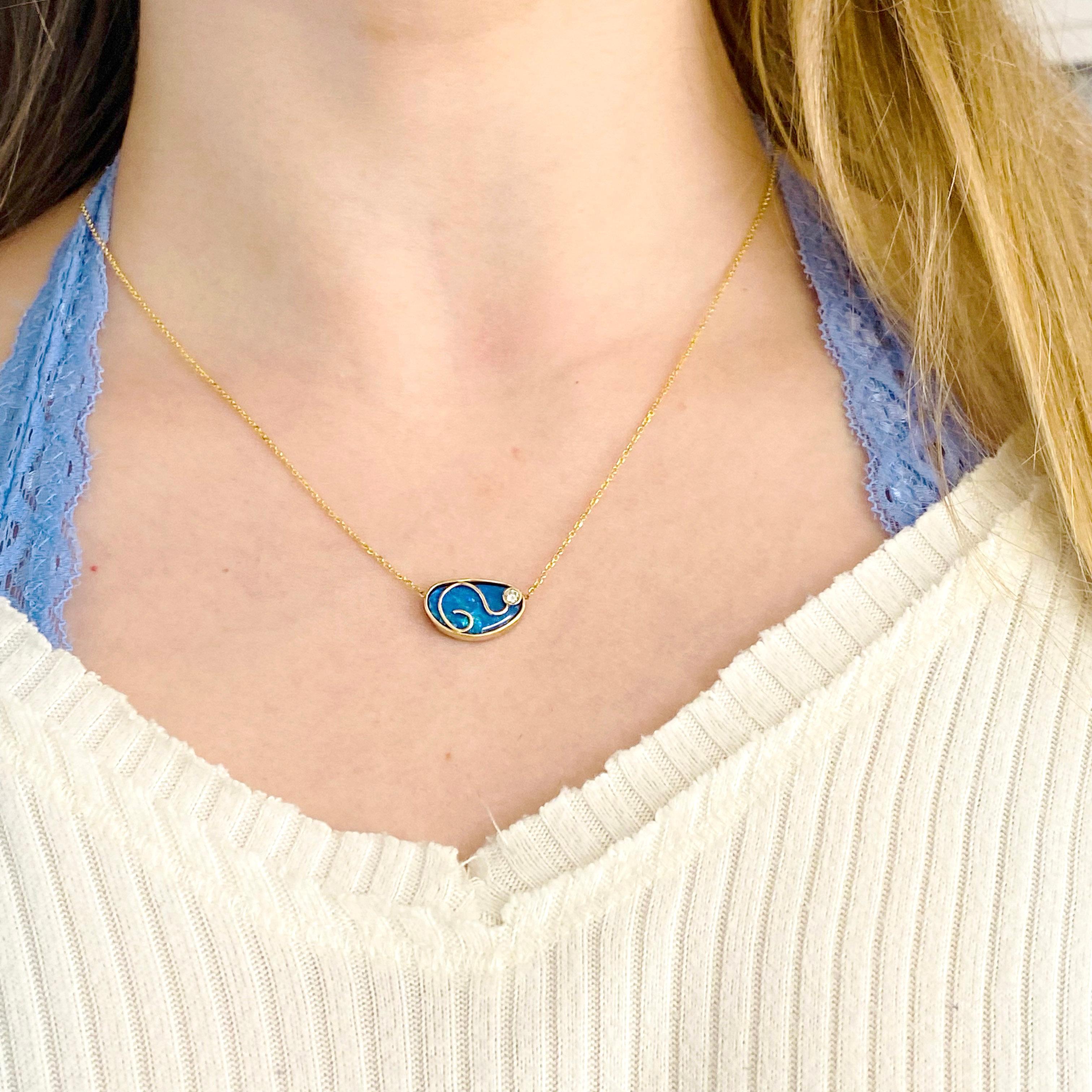 This opal and diamond necklace has been hand fabricated and is gorgeous on. It has a beautiful black opal in the center with a 14 karat yellow gold bezel around it. The blue fire of the opal is amazing and the designer chose to put a 14 karat gold