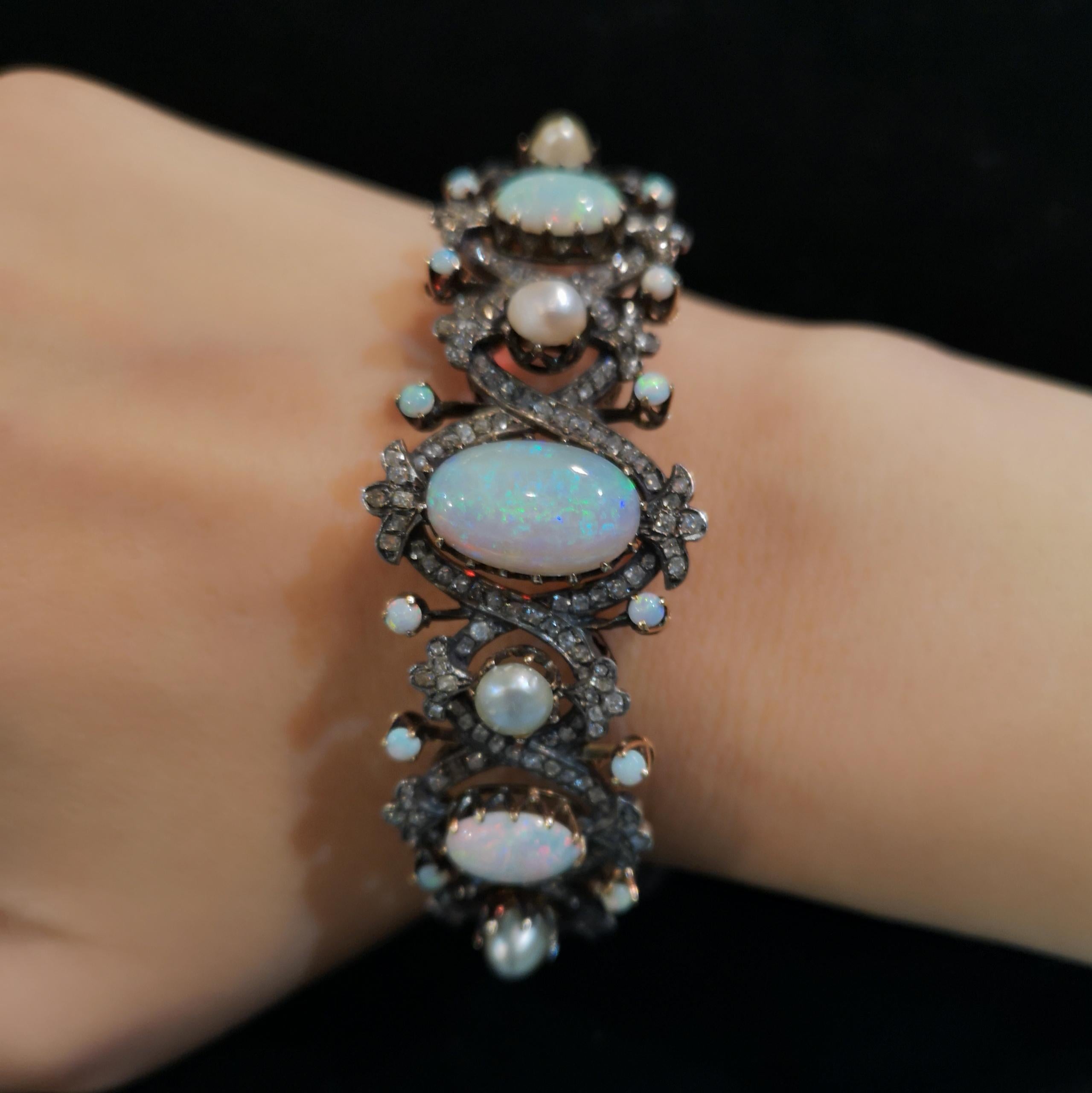 An opal, pearl and diamond bangle, set with three oval, cabochon cut opals, measuring 10 x 7.3mm, 15.2 x 9.3mm and 10.1 x 6.3mm, with four 5-5.5mm natural bouton pearls, surrounded by old-cut diamonds in a crossing over pavé style setting, with